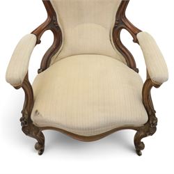 Late Victorian walnut open armchair, the carved shaped cresting rail centred by scrolls and foliage above a padded serpentine back and overstuffed seat upholstered in cream striped fabric, with padded scroll arms on open carved supports, raised on cabriole supports with carved knees and ceramic castors