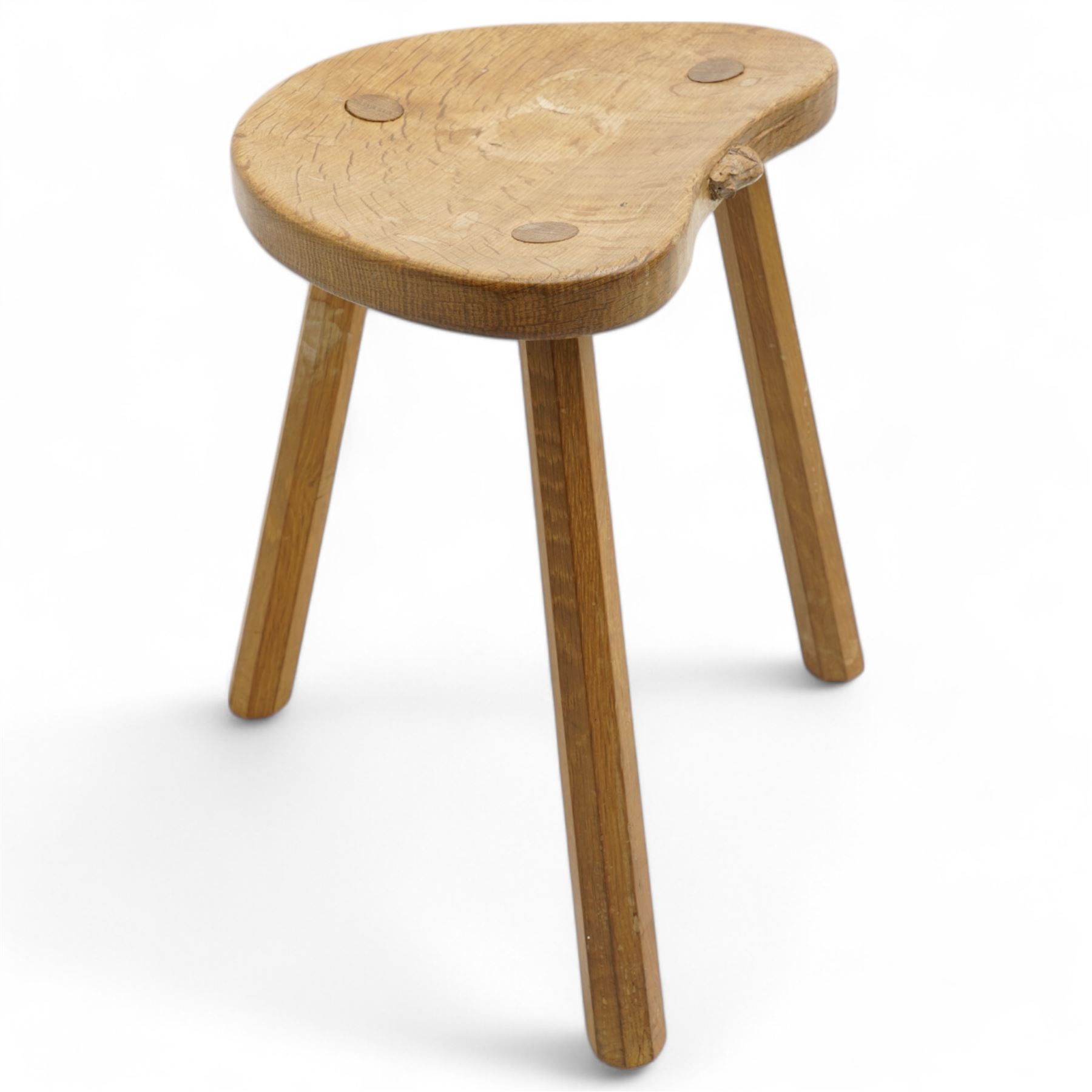 Mouseman - oak three-legged milking stool, dished kidney-shaped seat carved with mouse signature, on three octagonal tapered supports, by the workshop of Robert Thompson, Kilburn