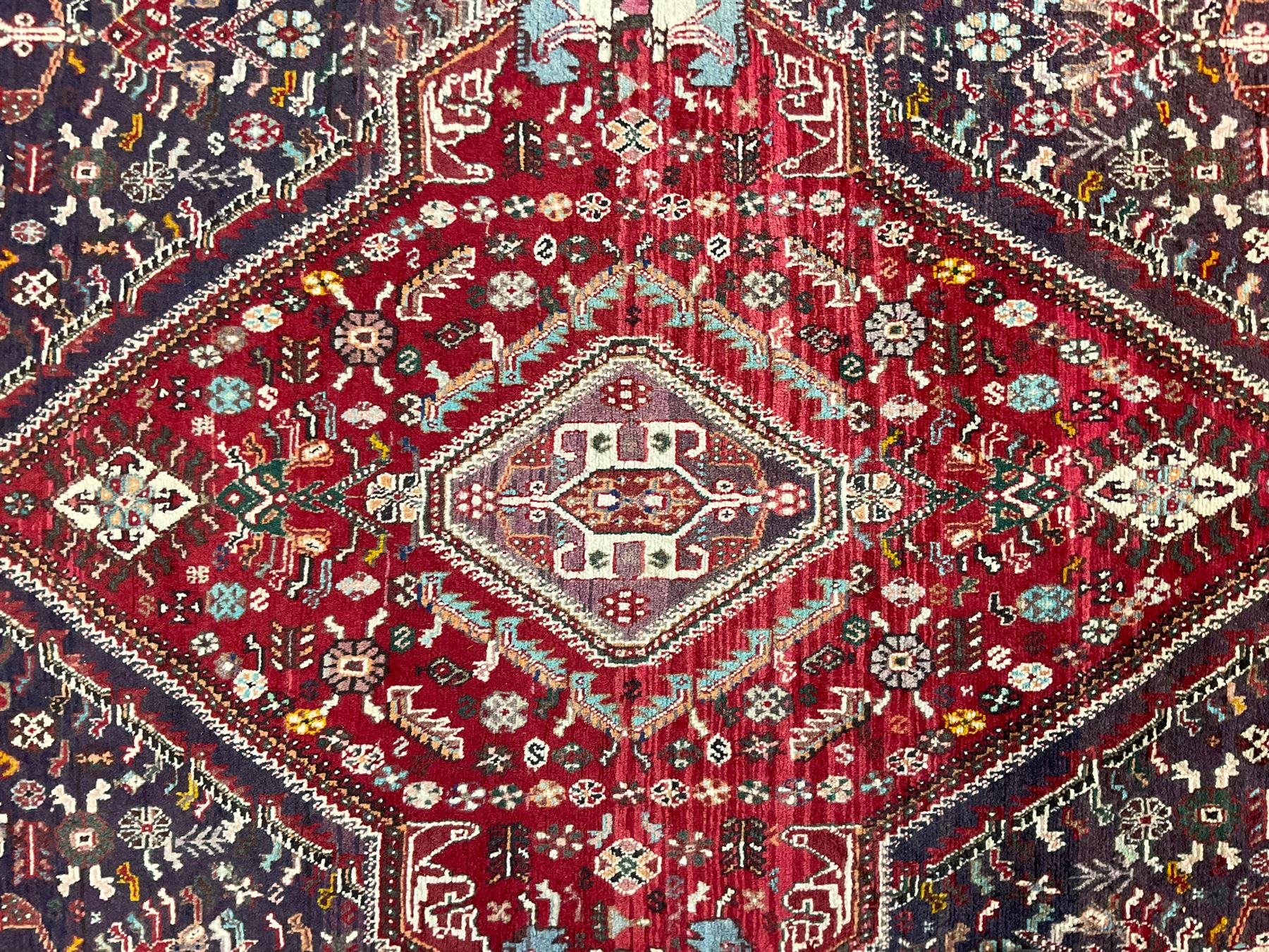 Persian Heriz crimson ground rug, field with large central lozenge surrounded by stylised plant motifs in a mauve background, guarded border with repeating foliage