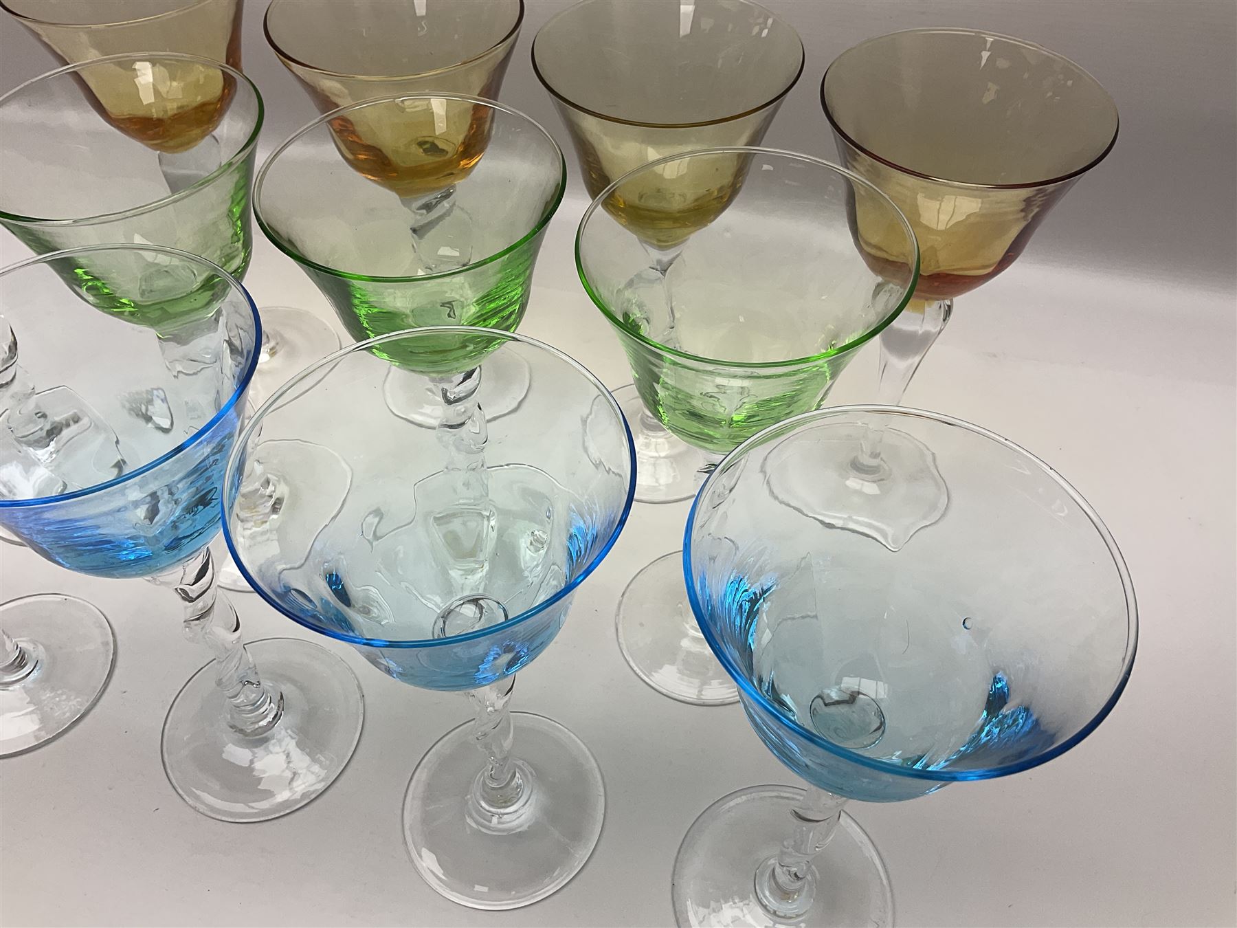 Ten coloured Adriana wine glasses by Abigails, to include blue, green, pink and yellow examples, each with part faceted bowl and twist stems, together with two similar orange examples with pulled stems, H24cm