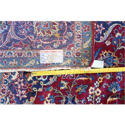 Central Persian Kashan hand-knotted carpet, crimson field with a central elaborate cusped medallion surrounded by elegant scrolling floral vine design incorporating stylized palmettes, rosettes and foliate sprays and similarly decorated spandrels enclosed by a dark indigo main border of floral arabesques between multiple guard stripes, cotton fringe ends 
