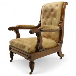 William IV mahogany gentleman's library reclining armchair, leather button upholstered and brass-studded back and seat, above leather-covered arms terminating with carved roundels and foliate scroll-carved ends, underside with brass mechanical trigger reclining lever, the apron with retractable foot rest, supported on lappet carved and turned legs with brass castors, circa 1835