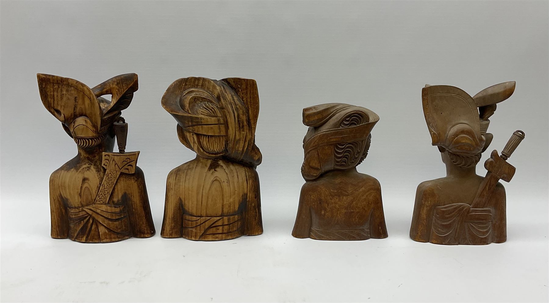 Two pairs of Balinese carved wooden bust figures of a man and woman, with elaborate head dresses, along with other wooden carved figures, a small barometer and a framed print. 