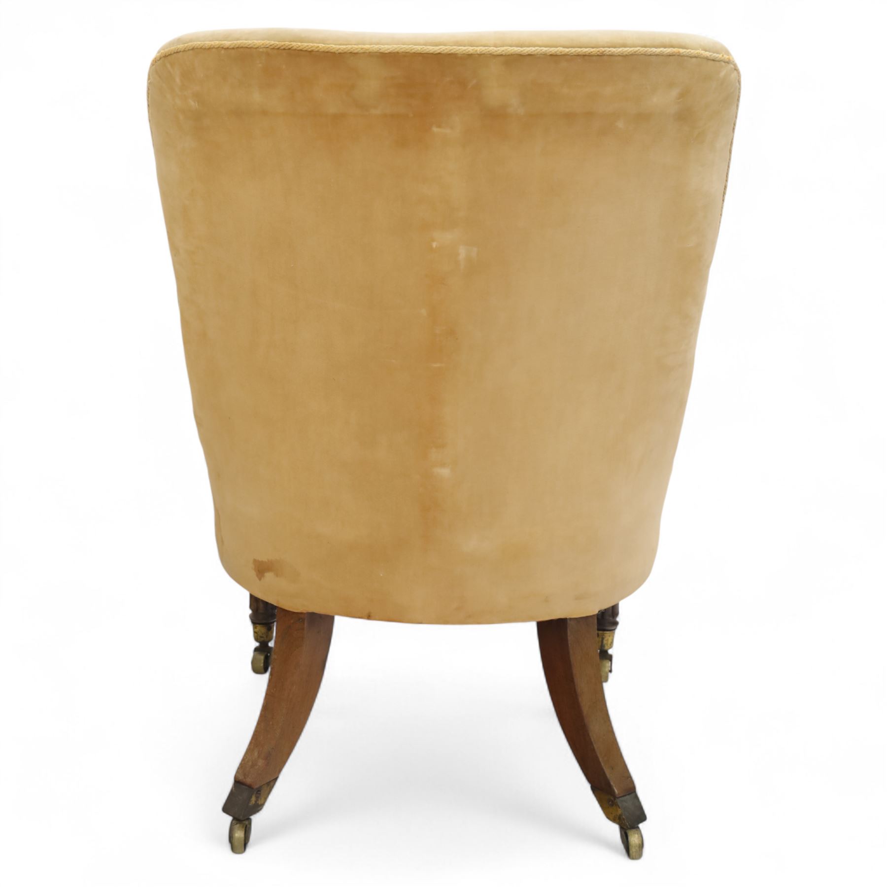 William IV mahogany library armchair, beige velvet upholstered back and padded seat with piping and scroll carved arms, reeded uprights, raised on tapered reeded front legs and out-swept back legs with brass castors 