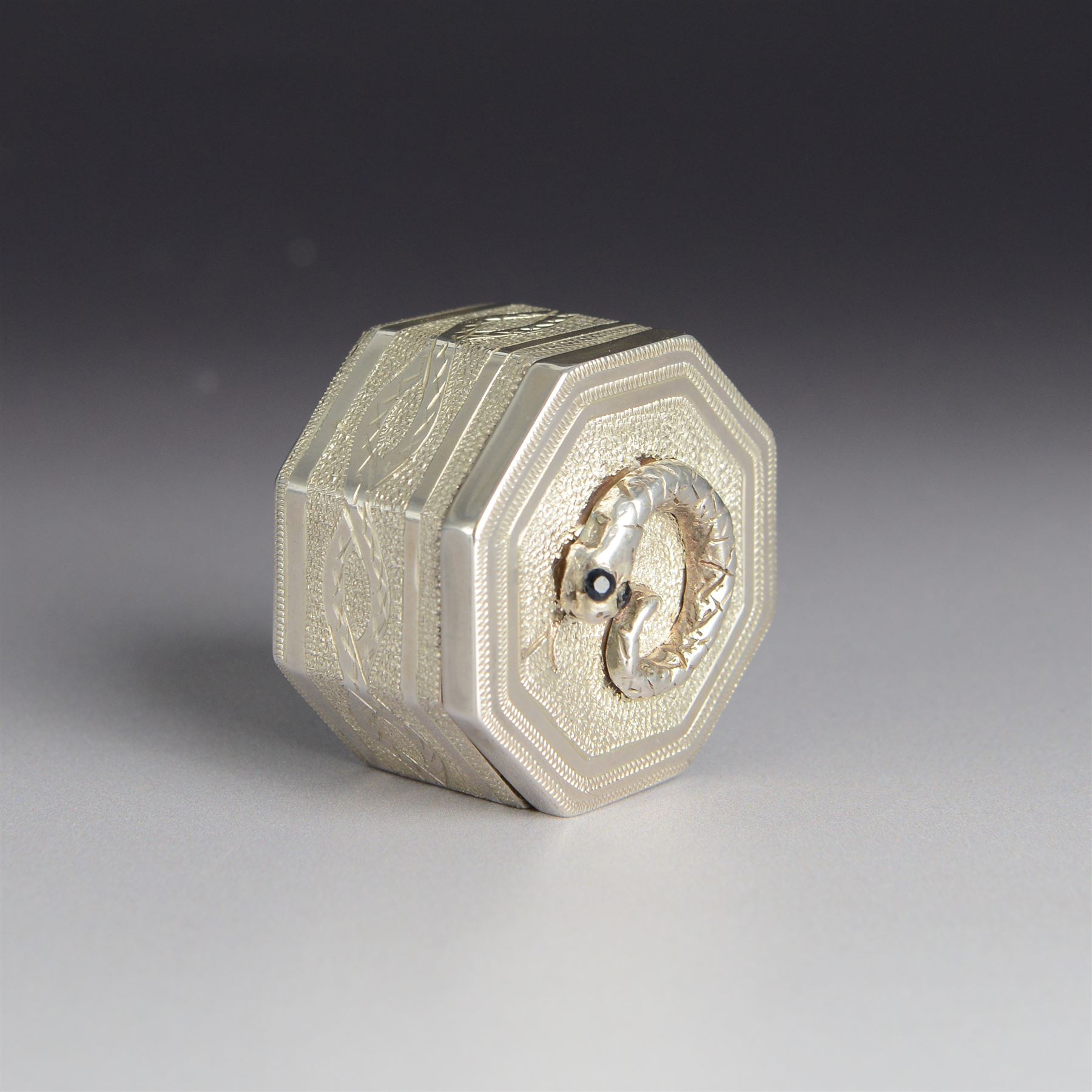 Silver trinket box, of hexagonal form, engraved with entwined snakes to body and decorated to the removable cover with a snake with sapphire set eyes, hallmarked Jonathan Braganza, London 2012, H3cm, W4cm
