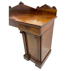 Early 19th century mahogany reverse break-front twin pedestal sideboard, raised back carved with cartouche and rosette detail with extending scrolling, fitted with two frieze drawers, the flanking panelled cupboards enclosing sliding trays and cellarette drawer