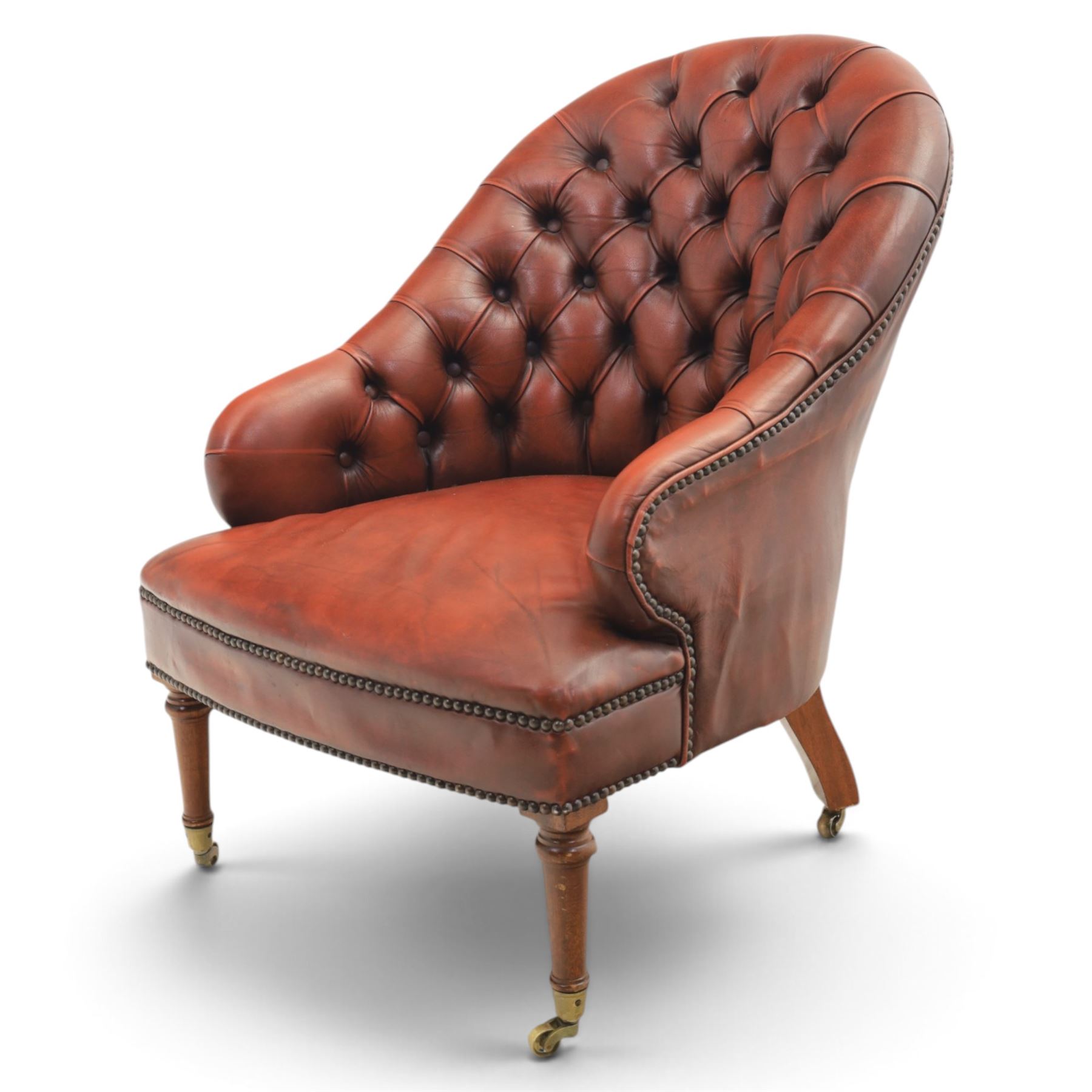 Victorian style oxblood leather armchair, deep button upholstered back and sides with rolled arms and brass studded borders, on turned front legs with brass and ceramic castors and splayed rear supports