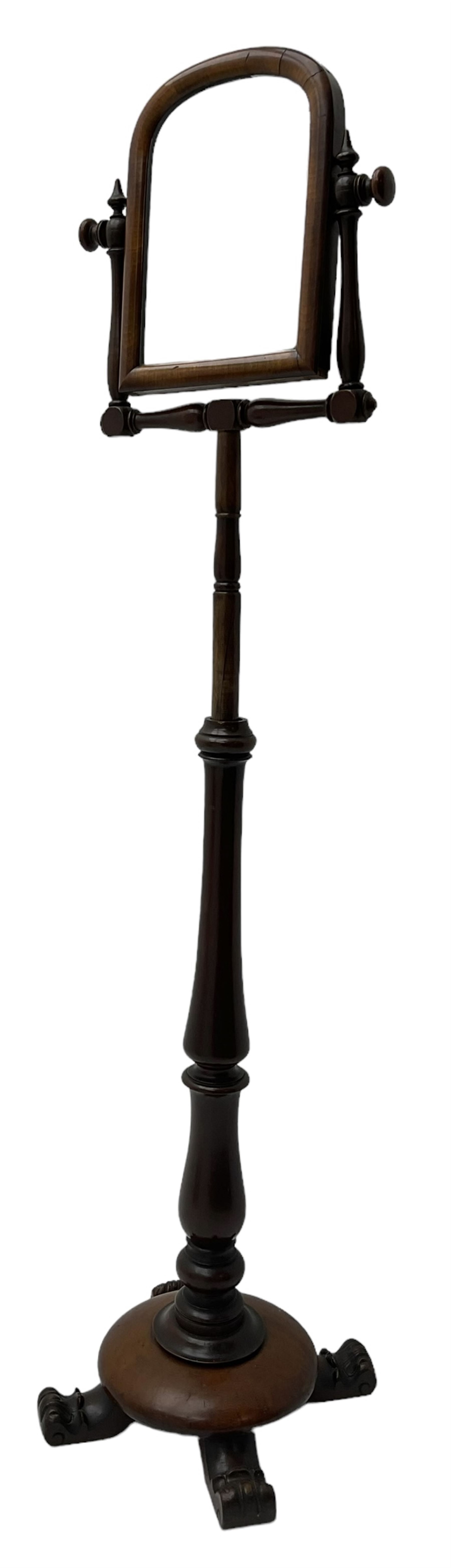 Early Victorian mahogany shaving mirror, arched frame with plain mirror plate on turned horns and supports, adjustable height mechanism on turned stem, circular platform base with four extending block feet carved with scrolled foliage 
