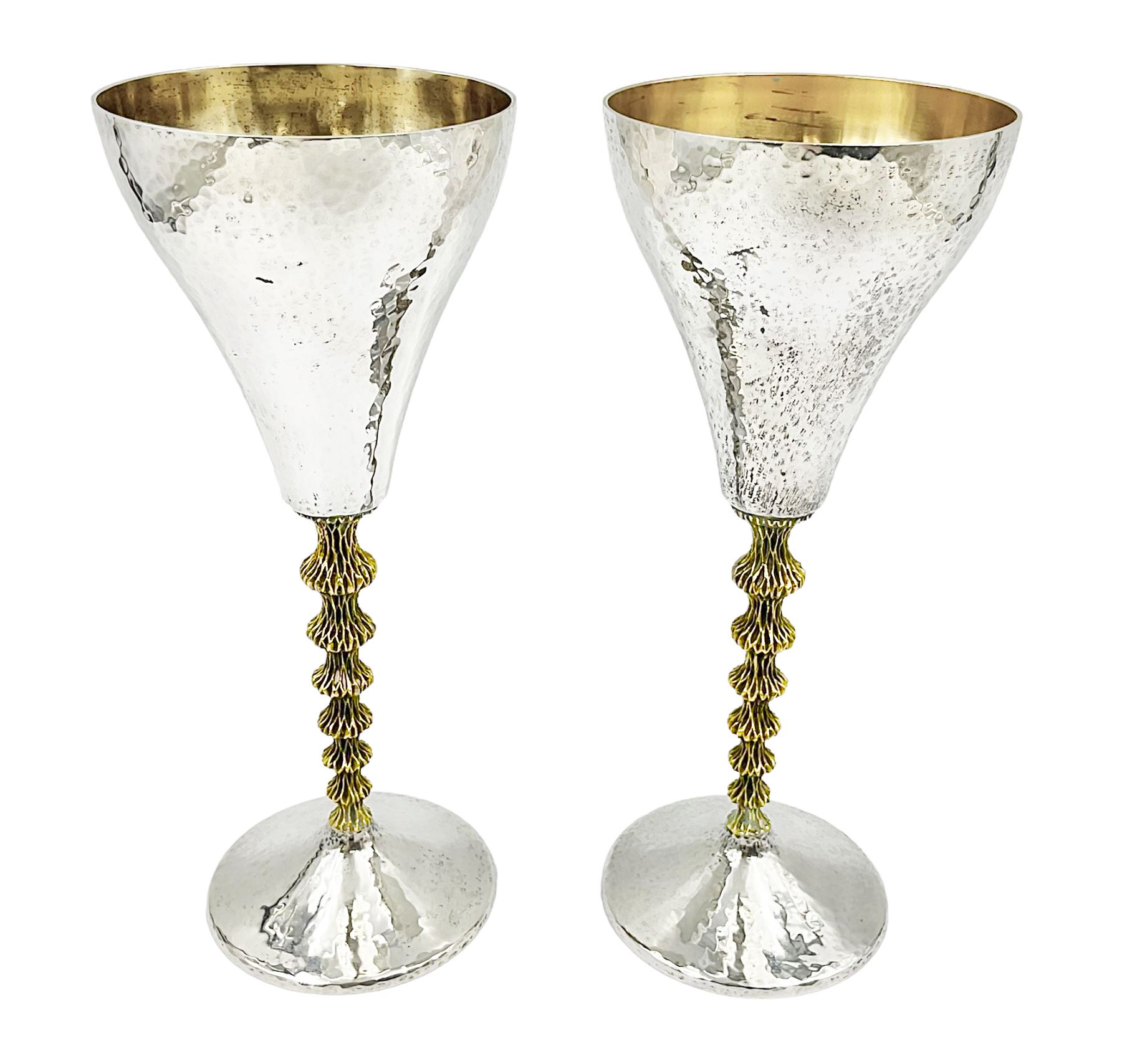 Pair of modern silver goblets by Stuart Devlin, the tapering cylindrical bowls each with spot hammered decoration and gilt interiors, the parcel gilt stems with signature textured detailing and six graduating knops, upon conforming spreading circular foot, hallmarked Stuart Devlin, London 1976, H17.7cm