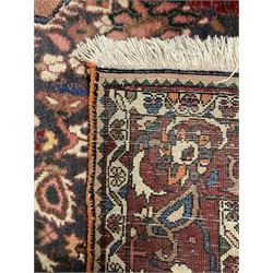 Persian Meshed red ground carpet, the cusped field profusely decorated with stylised flower head and plant motifs, the guarded border with scrolling foliate design
