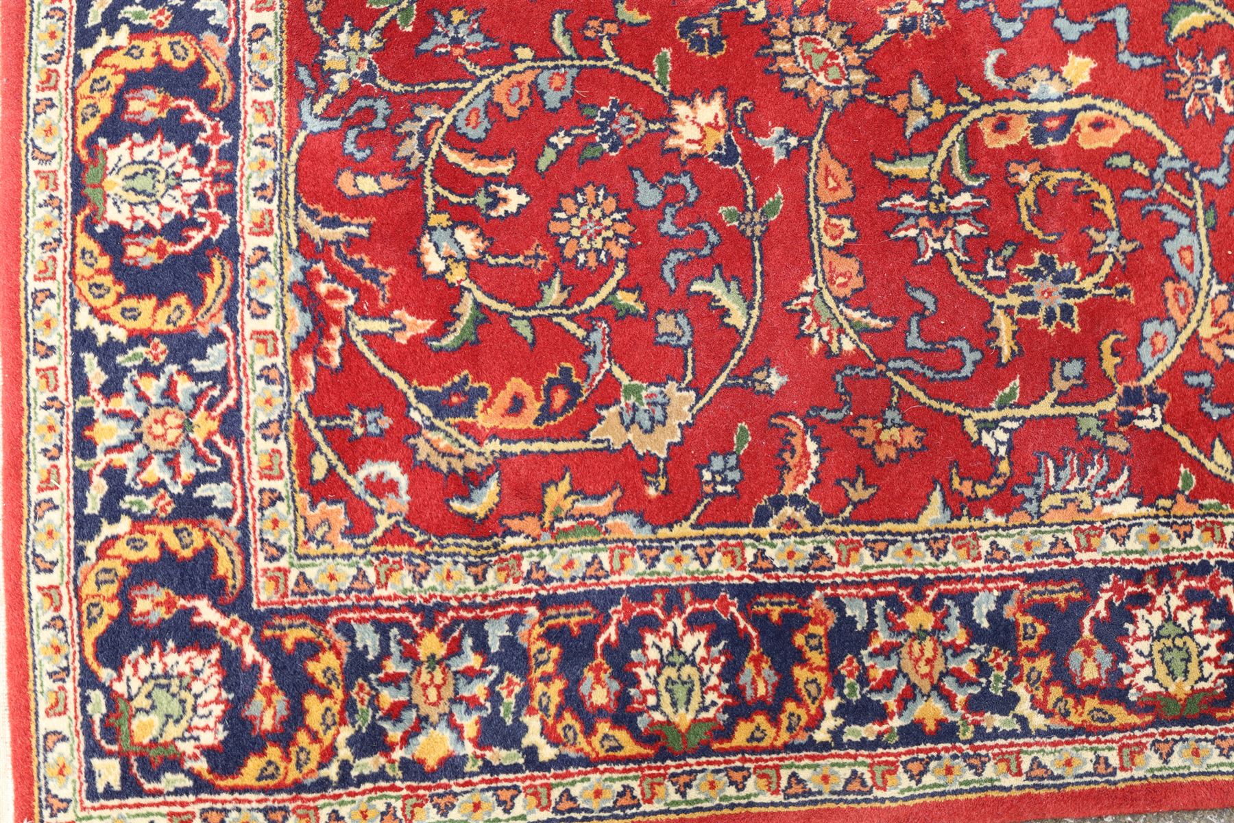 Persian Kashan crimson ground rug decorated with scrolling foliage, the indigo guard stripes with repeating stylised palmette motifs