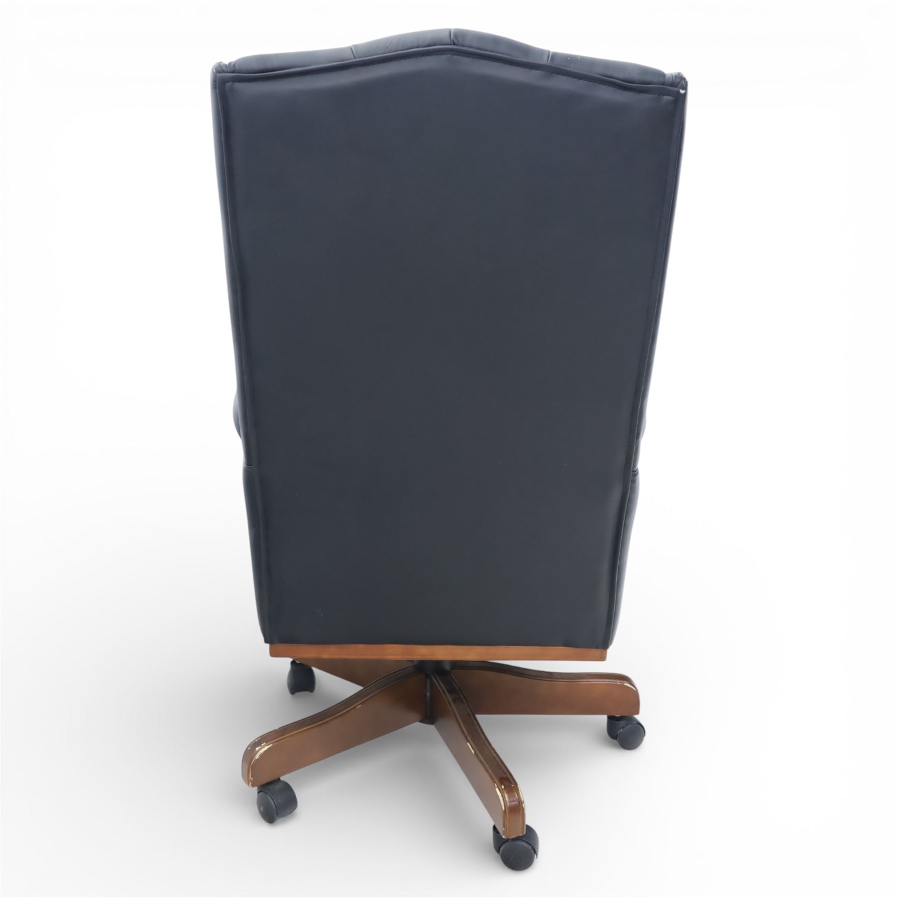 Chesterfield style desk chair upholstered in black, brass studded trim with tall button backed seat, with faux wooden base raised upon castors