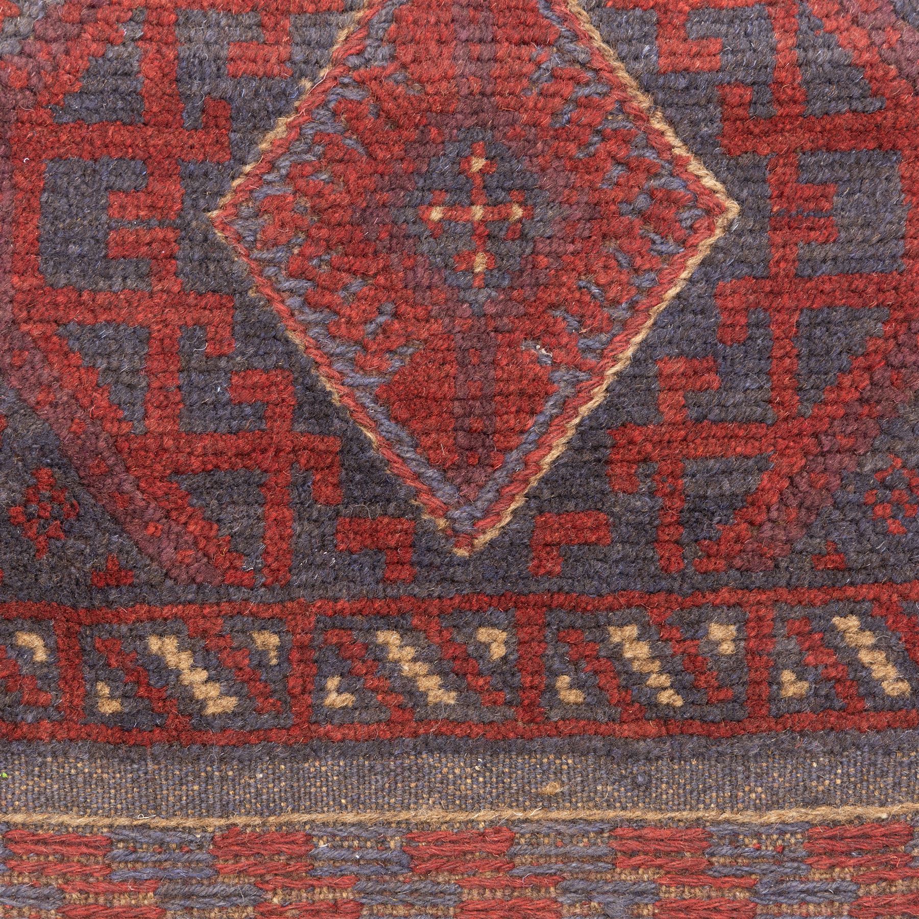 Afghan hand-knotted wool runner, dark red and indigo blue madder, with a repeating central diamond medallion design within multiple geometric borders, with flatweave ends 