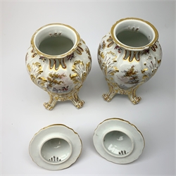 A pair of Continental porcelain vases and covers, each of baluster form raised upon four scroll feet, with pierced bud finial covers, the bodies painted with landscape and figural scenes and further detailed with flowers and heightened with gilt, with gold Hochst style mark beneath,  H22.5cm. 