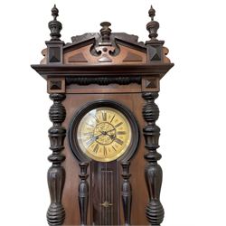 Late 19th cent German wall clock in a mahogany and ebonised case with turned columns and finials, eight-day spring driven movement striking the hours and half hours on a gong, ivorine chapter with a gilt repousse centre, glazed door with a visible gridiron pendulum.