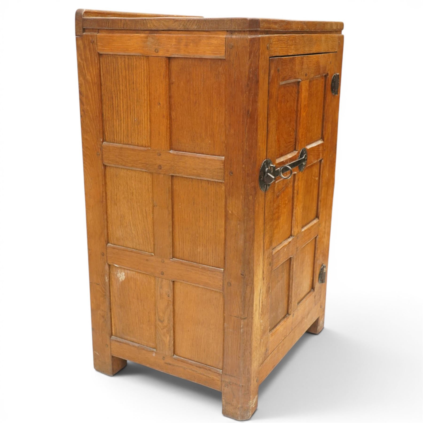 Mouseman - early-to-mid-20th century adzed and panelled dark oak bedside cupboard, raised back over rectangular canted top, fitted with single panelled cupboard door with chamfered rails and wrought iron fittings, enclosing two adjustable shelves, raised on canted square feet, carved with mouse signature, by the workshop of Robert Thompson of Kilburn