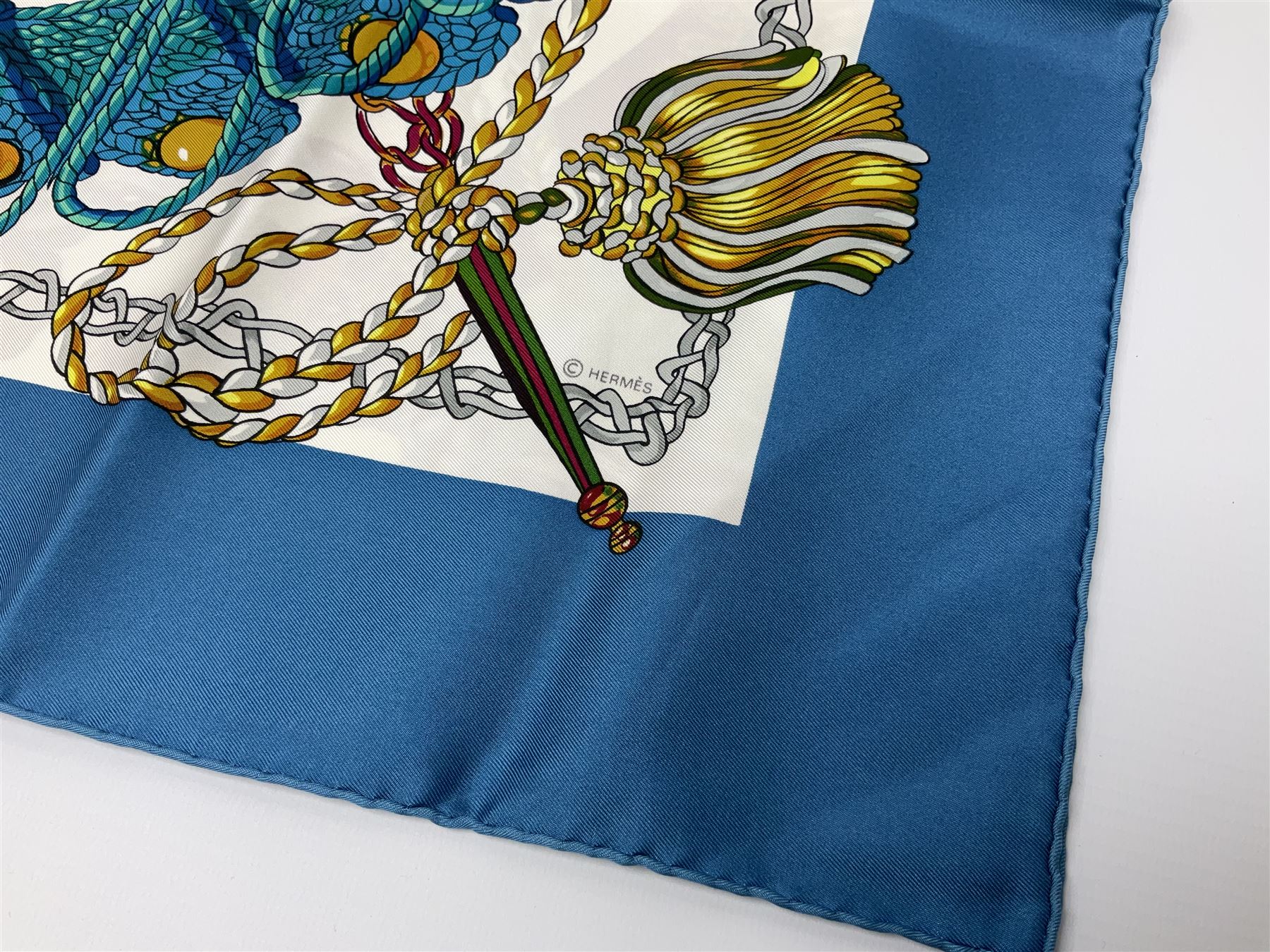 Hermès 'Le Timbalier' silk scarf, designed by Francoise Heron in 1961, printed with a central image of a gentleman on horseback donning extravagant dress, on white ground surrounded with colourful stylised knotted ropes, contained within peacock blue border, with rolled hand stitched edges and Hermes material label, 87cm square