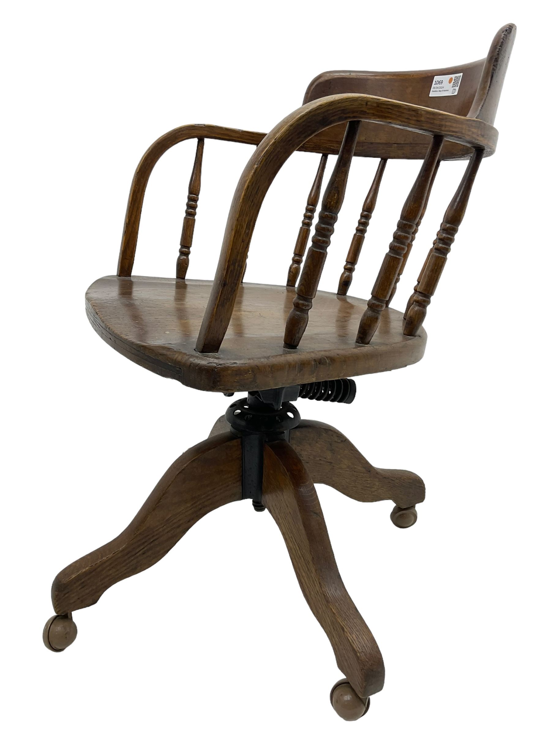 Early 20th century oak framed swivel Captain's chair, tub shaped back with turned spindle supports over saddle shaped seat, quadriform base on castors