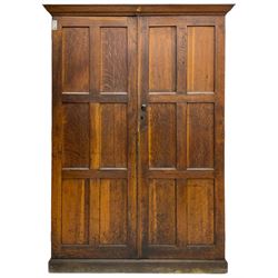 The North of England School Furnishing Company Limited Darlington - early 20th century oak school cupboard, projecting moulded cornice over two panelled doors, fitted with shelves, on chamfered plinth base 
