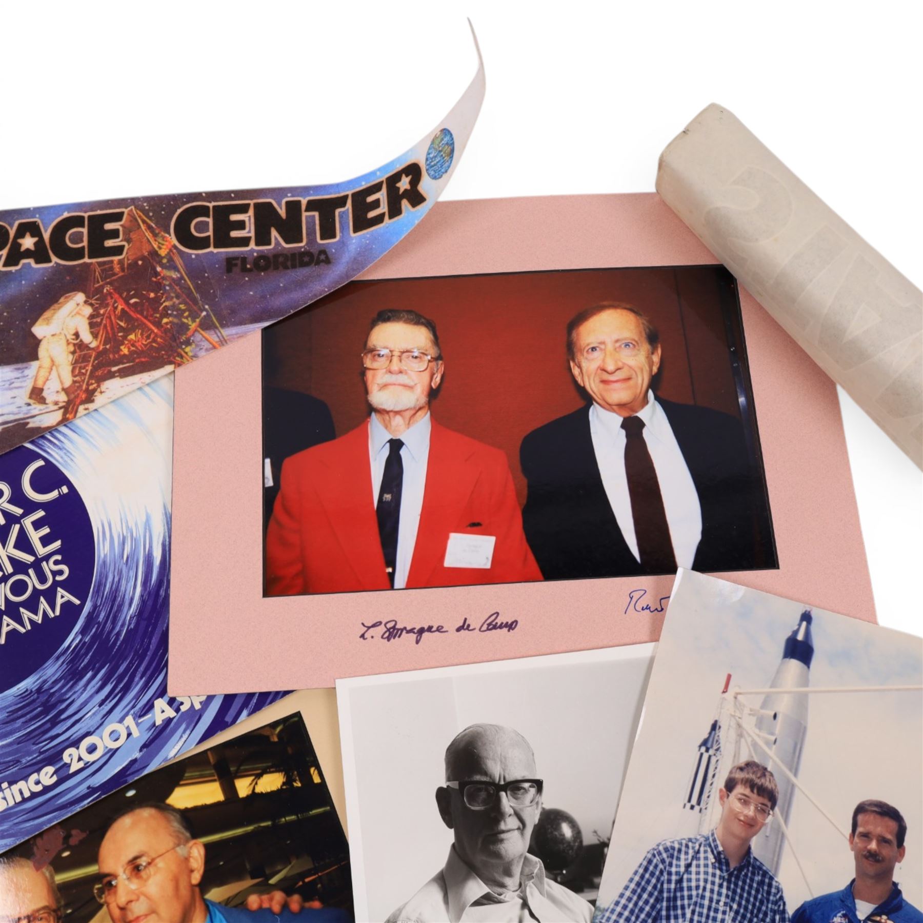 Collection of ephemera relating to Arthur C Clarke, including colour photograph of Arthur with author Joe Green, Jay Kubica and astronaut Chris Hadfield at NASA Kennedy Space Centre, Kennedy Space Centre pennant flag, colour photographs of authors Sam Moskowitz with Forrest Ackerman and L. Sprague de Camp with Robert Bloch, all signed below by the authors, a black and white photograph of Arthur for his 13-Part ITV series 'Arthur C Clarke's Mysterious World', Pan Books cardboard advertisement for Rendezvous with Rama and an Evening Standard poster for The Other Side of the Sky

Notes: This item is from the private collection of Arthur C. Clarke's brother.