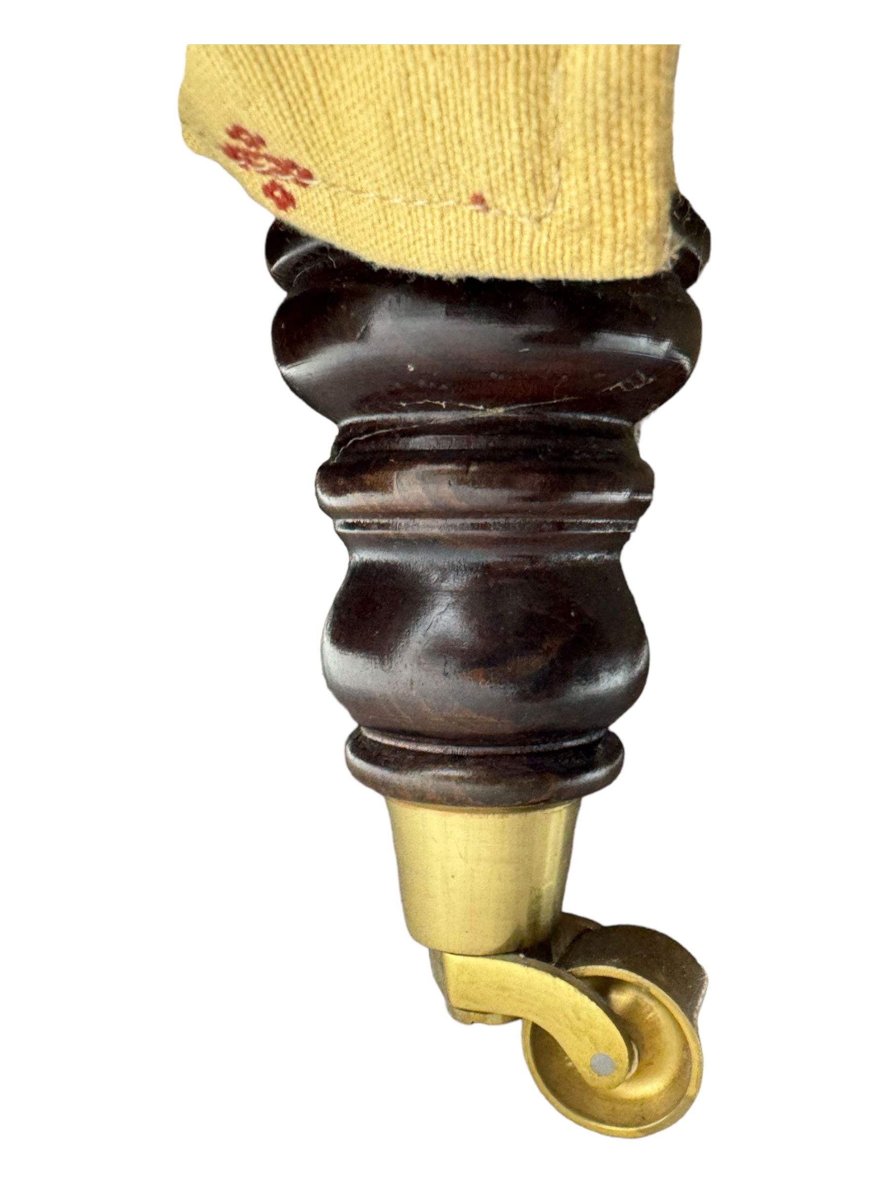 20th century Knole design two seat sofa, high back and double drop-arm joined by mahogany finials and ties, upholstered in camel ground fabric with red lozenge design, on turned supports with brass castors