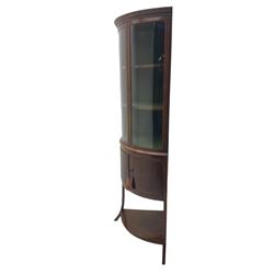 Edwardian mahogany bow front standing corner cabinet, projecting cornice with Greek key moulding decoration, two glazed doors with ebony and satinwood stringing enclosing two shelves, over cupboard and under-tier 