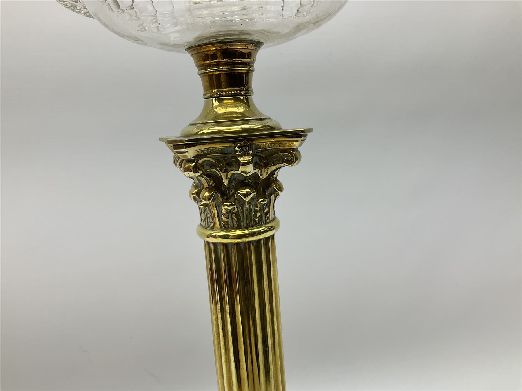 Victorian brass oil lamp, the square stepped base leading to a Corinthian column supporting a part slice cut clear glass reservoir, burner, clear glass chimney and foliate etched glass shade with amber rim, overall H80cm