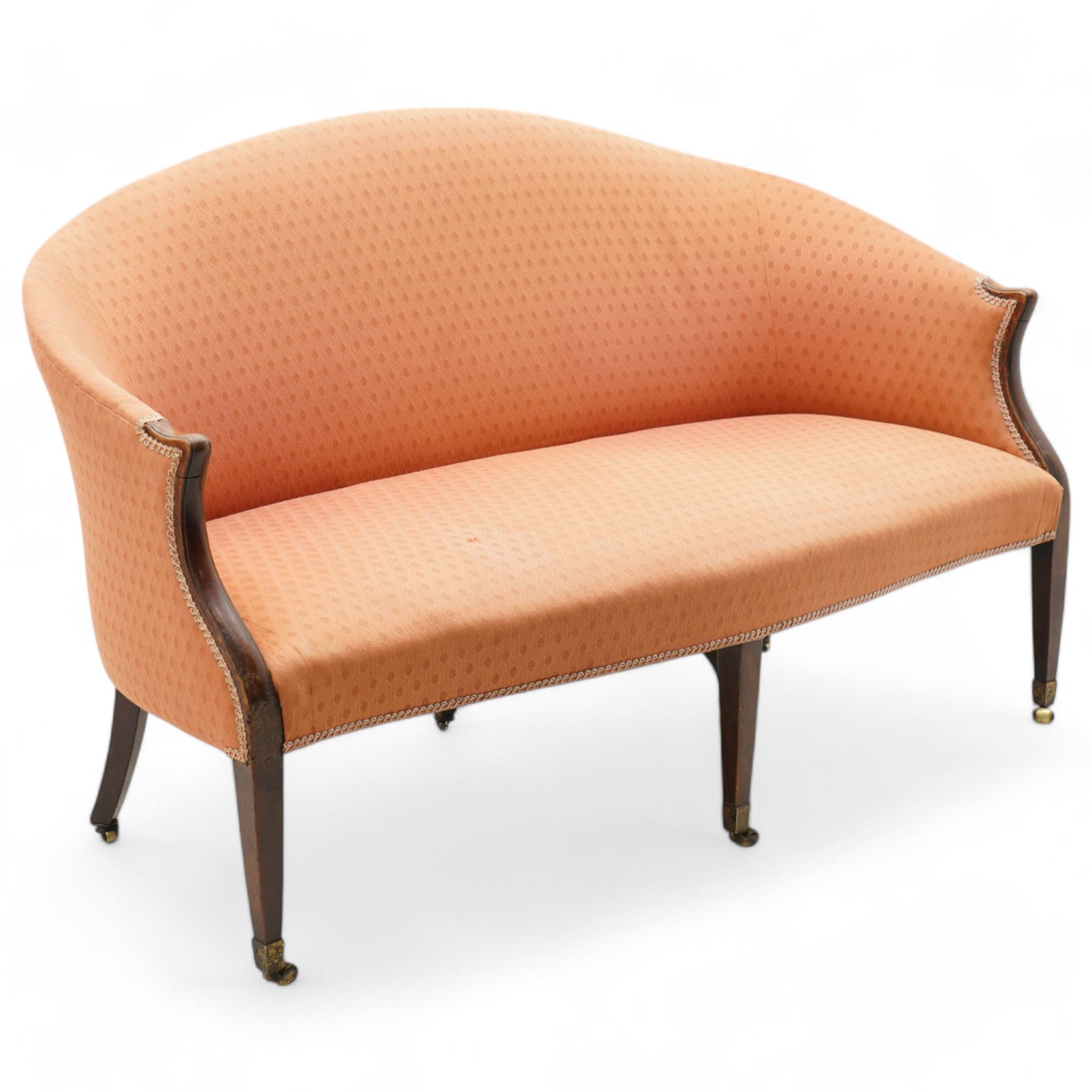 George III Hepplewhite design settee, arched back over serpentine set, upholstered in salmon fabric with repeating pattern, on square tapering supports with brass cups and castors 