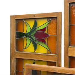 Collection of leaded stained glass window panes in mahogany frames, depicting central stylised tulip flower in green and red within an amber and yellow field, mottled and plain glass, in various sizes (single panes: 118cm x 62cm & 127cm x 62cm; triptych panes: 182cm x 62cm & 194cm x 62cm & 196cm x 62cm; four panel pane: 209cm x 62cm; smallest single panel: 43cm x 62cm)