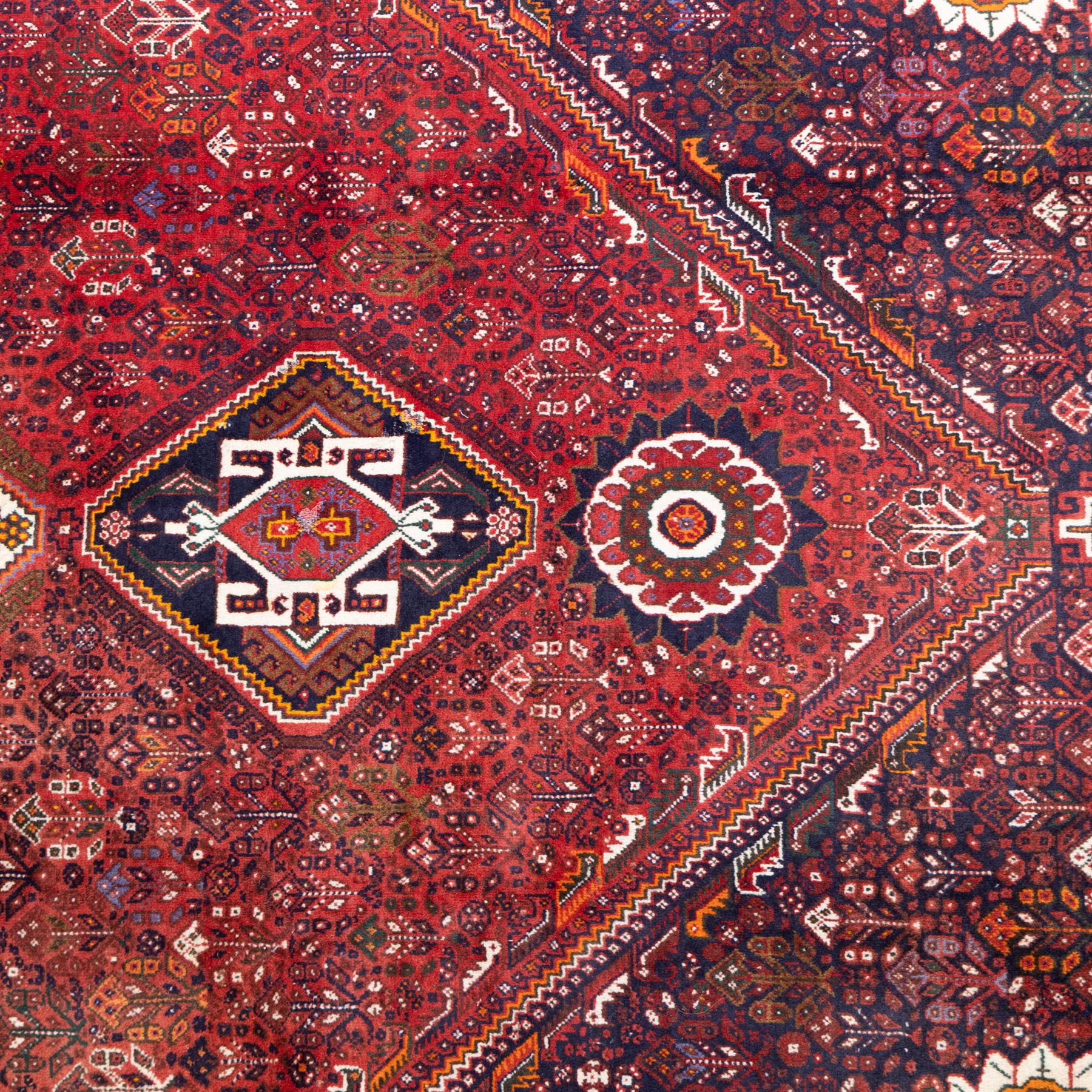 Qashqai wool carpet, red diamond-shaped field decorated with three stepped pole medallions, floral rosettes and scattered stylised motifs, within dark blue spandrels and multiple geometric guard borders