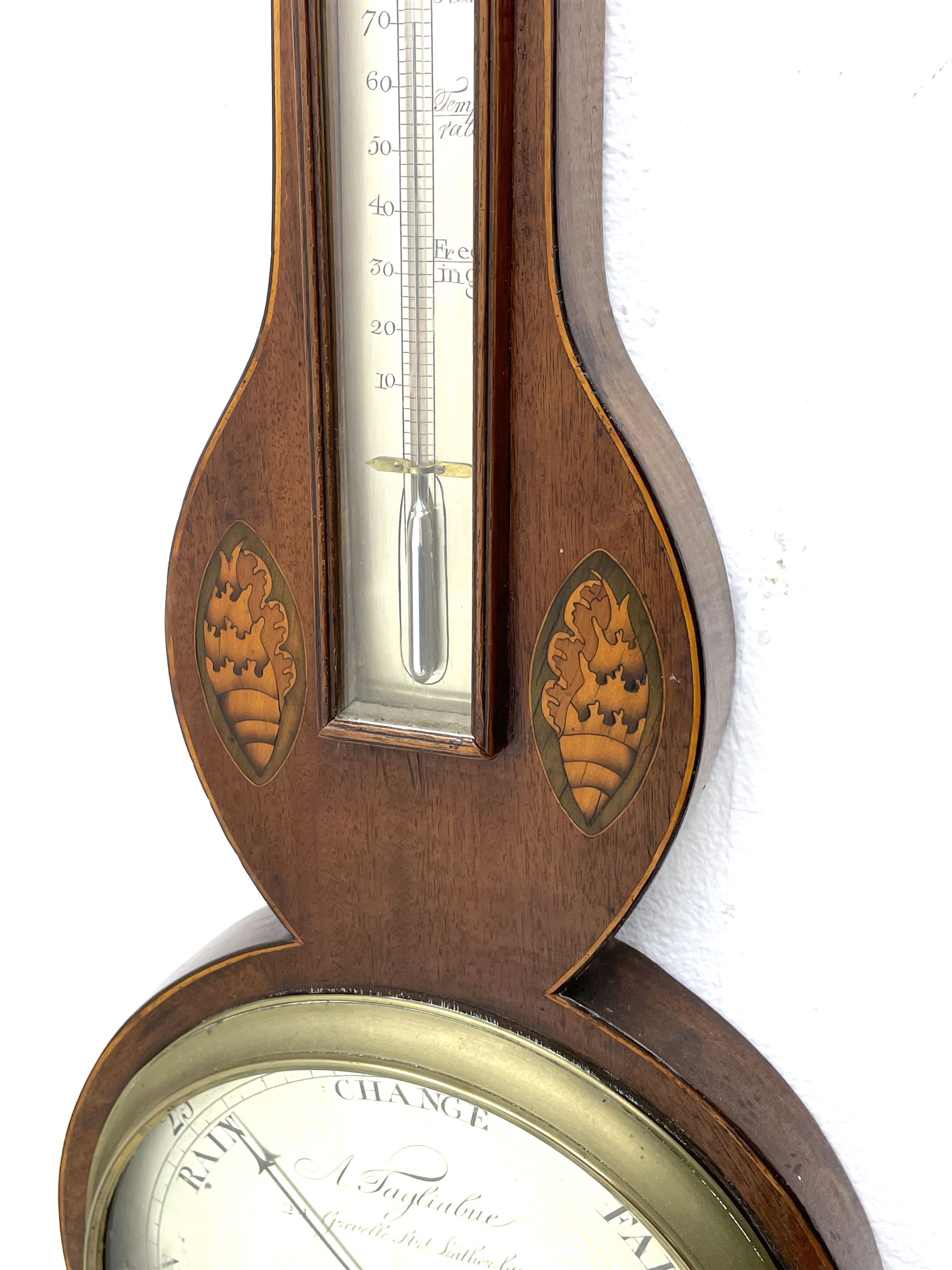 Early 19th century William IV mercury wheel barometer with a rosette inlaid broken pediment and correspondingly inlaid round base, mahogany veneered case with inlaid oval conch shell paterae and satinwood stringing to the edge, with an arched thermometer box and spirit thermometer measuring degrees Fahrenheit from 20 to 120, eight-inch silvered register reading barometric pressure in inches from 28  to 31, with predictions in Roman upper and lower case and script, dial inscribed “A Tagliabue,24 Grenville Street, Luther Lane, London”, with a steel indicating hand, brass recording hand and cast brass bezel.