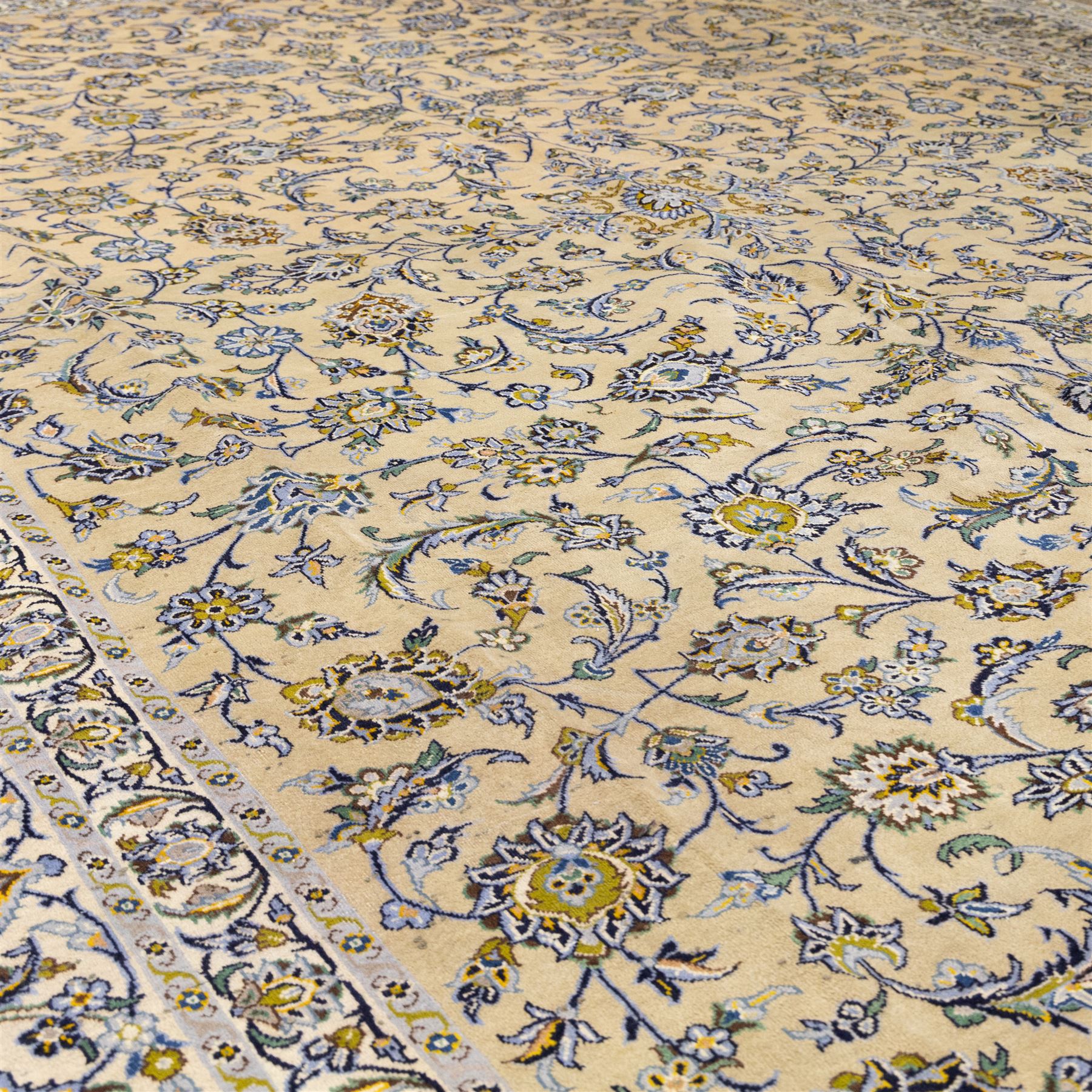 Central Persian Kashan hand-knotted carpet, pale ivory ground, decorated with an all-over scrolling floral design of palmettes rosettes, and leafy vine work enclosed by a wide floral border and multiple guard borders in tones of soft blues, sage green, muted gold, and ivory, with cotton fringe ends