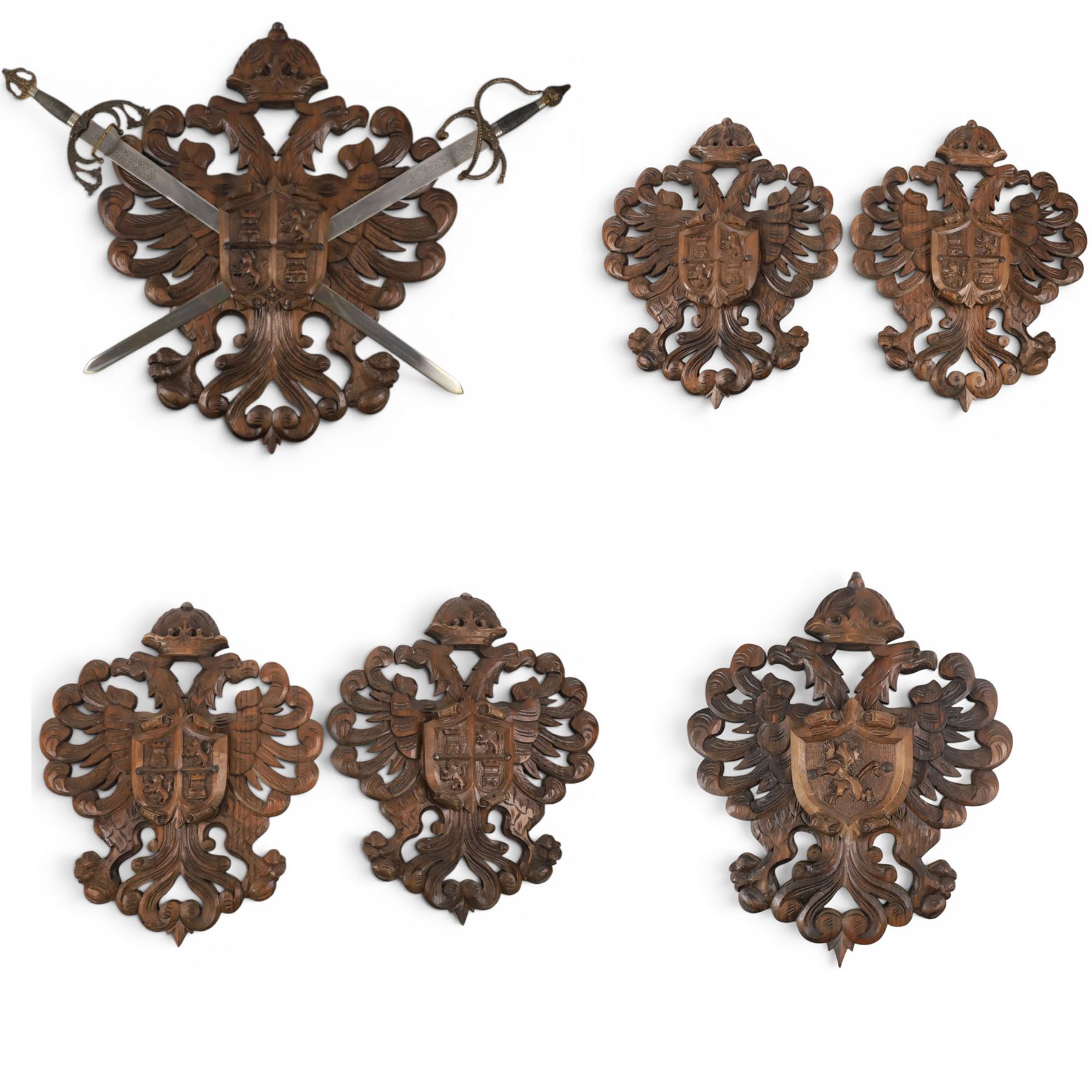 Carved wooden wall plaque, decorated with foliate scrolls, with two reproduction swords attached, together with five other wooden plaques with foliate scrolls and shields