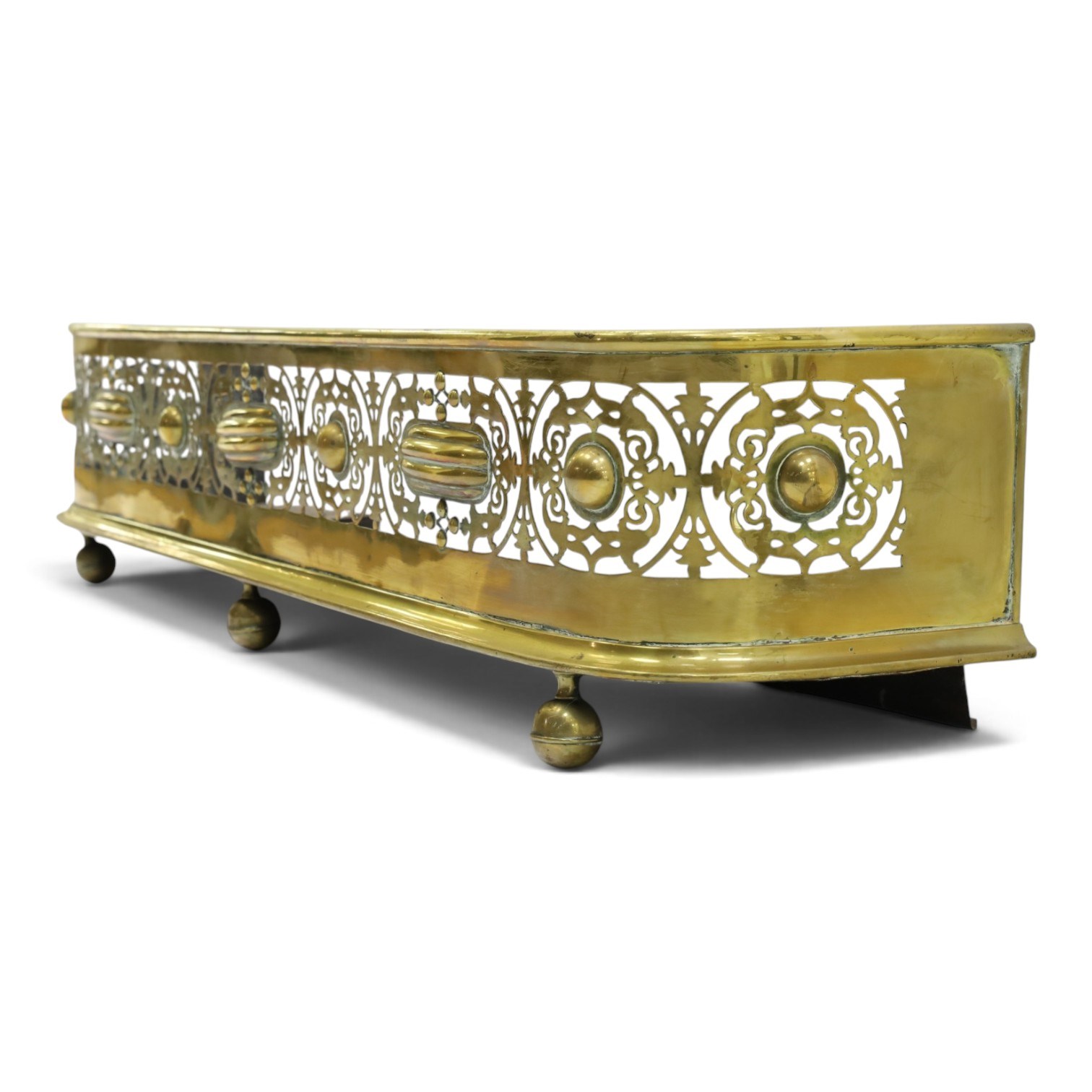 Victorian pierced brass fire fender, the pierced scrolling gallery of Aesthetic taste with applied roundels and protruding lobed mounts, raised on bun feet