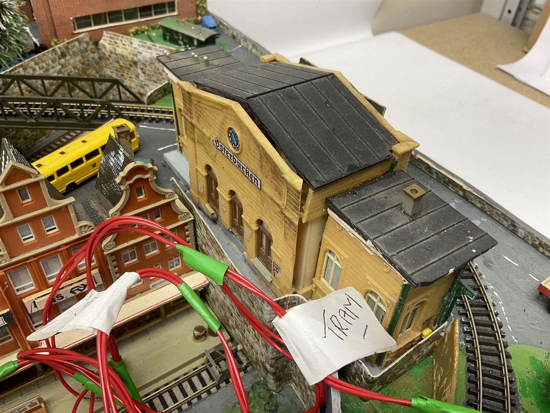 Table top 'N' gauge continental scenic layout as a split level town with various loops of track, station with numerous platforms, engine shed, assorted buildings, roads with motor vehicles and figures, tunnels, trees, river with bridge, tram depot etc 122 x 52cm