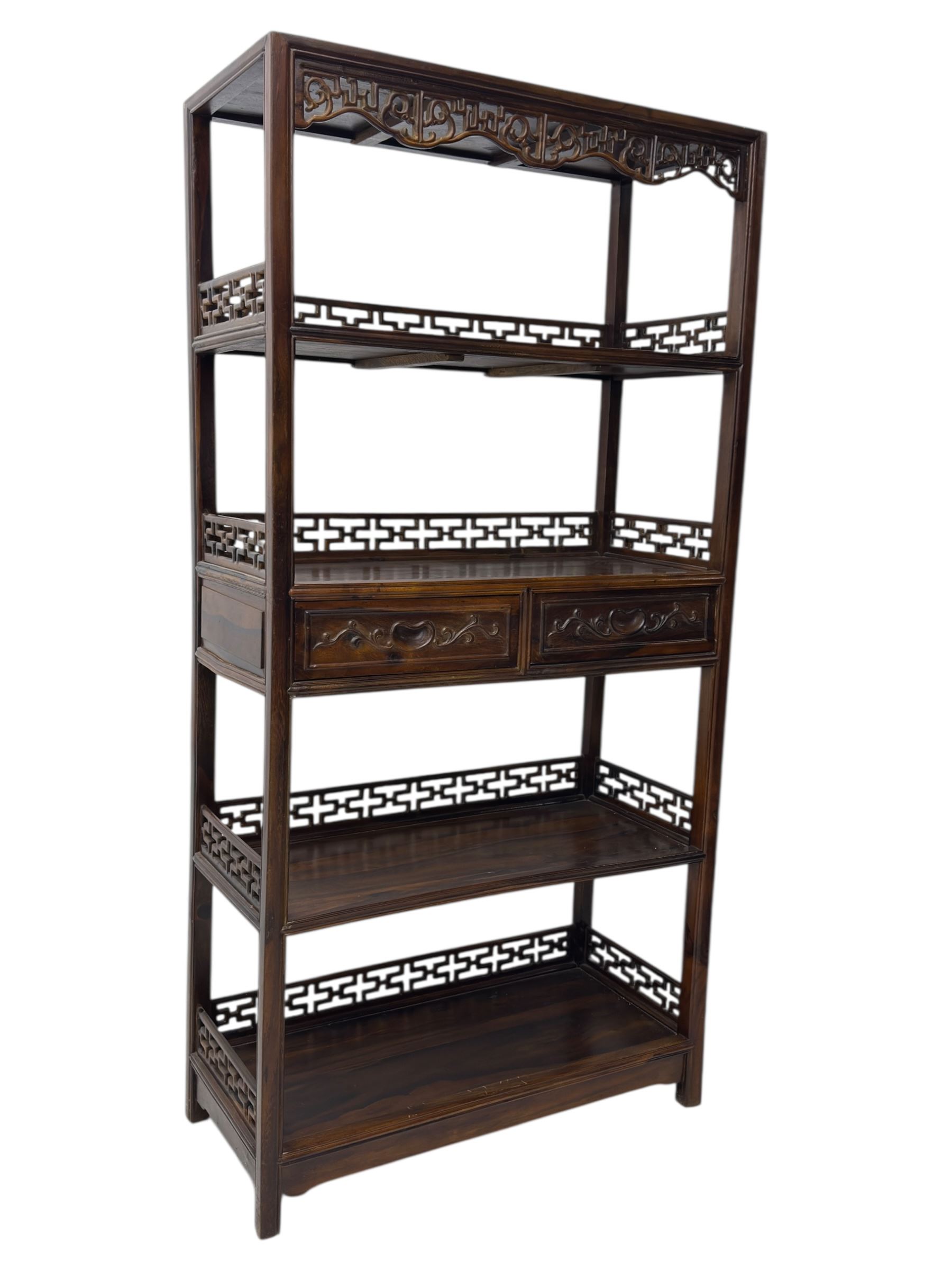 Early 20th century Chinese hardwood display étagère bookcase, the rectangular open tiered frame with pierced frieze and geometric openwork gallery to each shelf, fitted with two short drawers carved with stylised lotus motifs, supported on square uprights with pierced apron and integral gallery rails