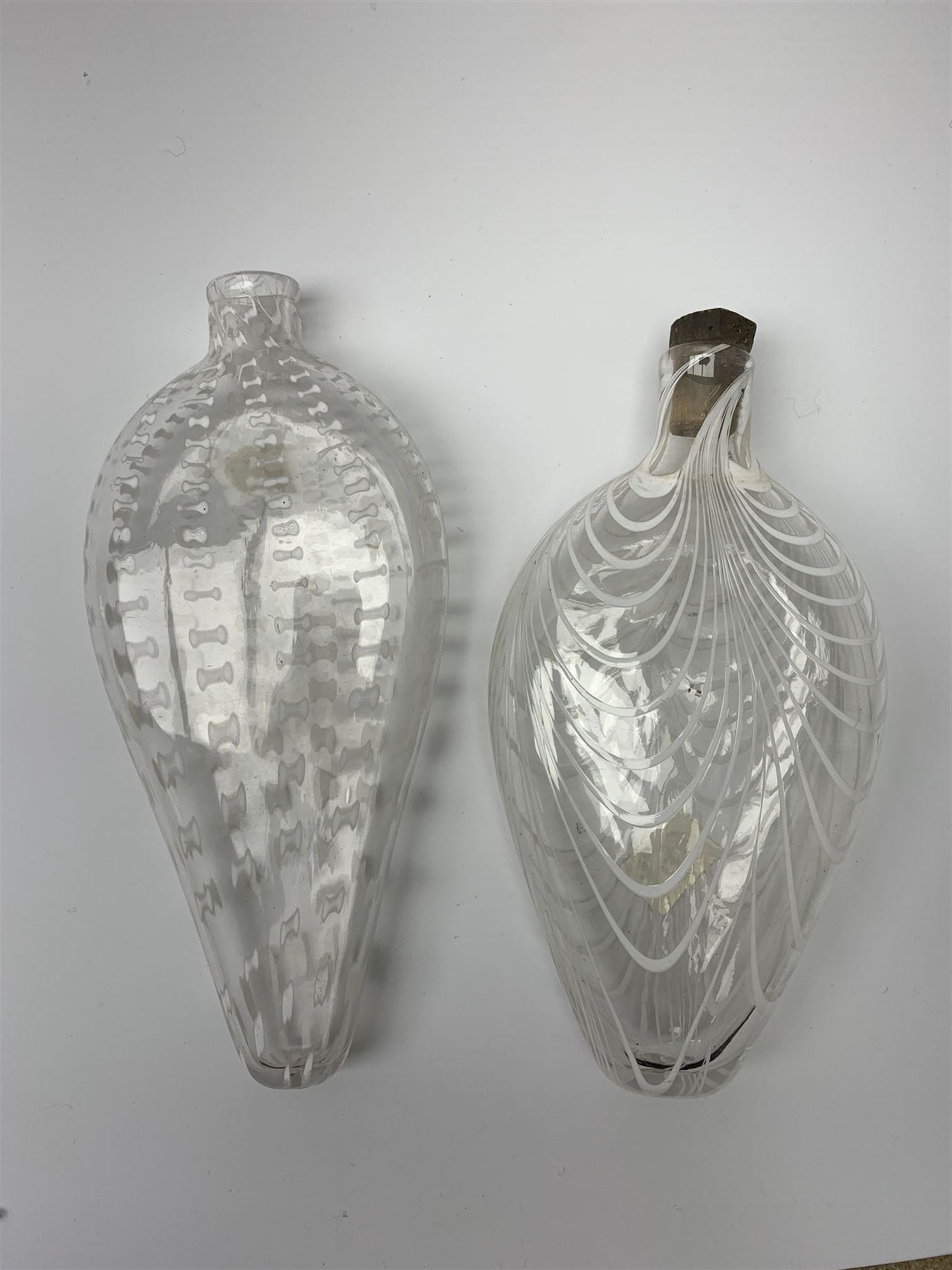 19th century Nailsea glass flask of compressed ovoid form, the clear body with opaque white combed decoration, H21cm, together with another similar example decorated with enamelled stylised bands, H23cm