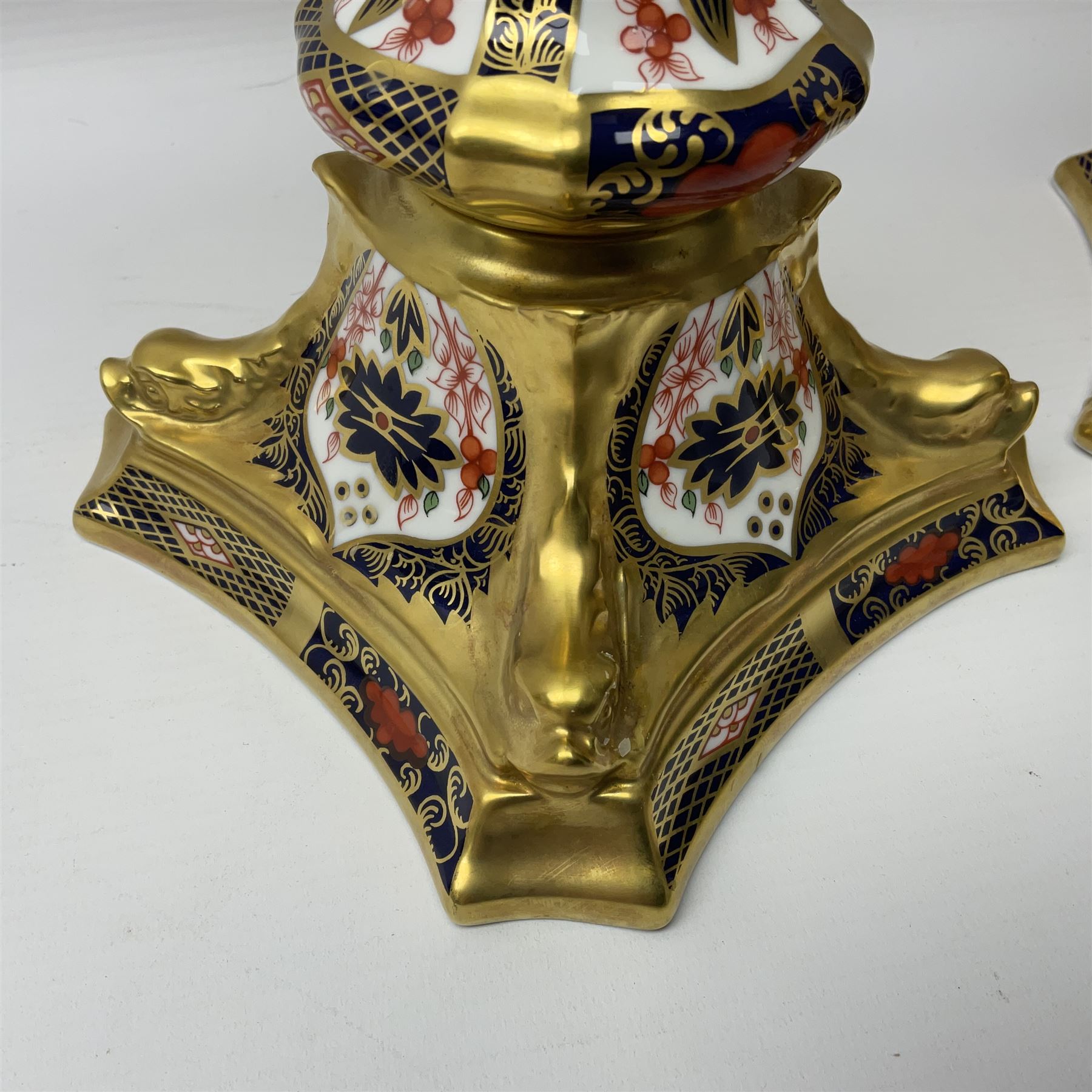 Pair of modern Royal Crown Derby Old Imari 1128 pattern candlesticks, each with shaped drip tray affixed to squat socket, upon spreading stem and canted square base with gilt dolphin edges, with printed marks beneath including Roman numeral year cypher for 2003, H26.5cm, with original boxes