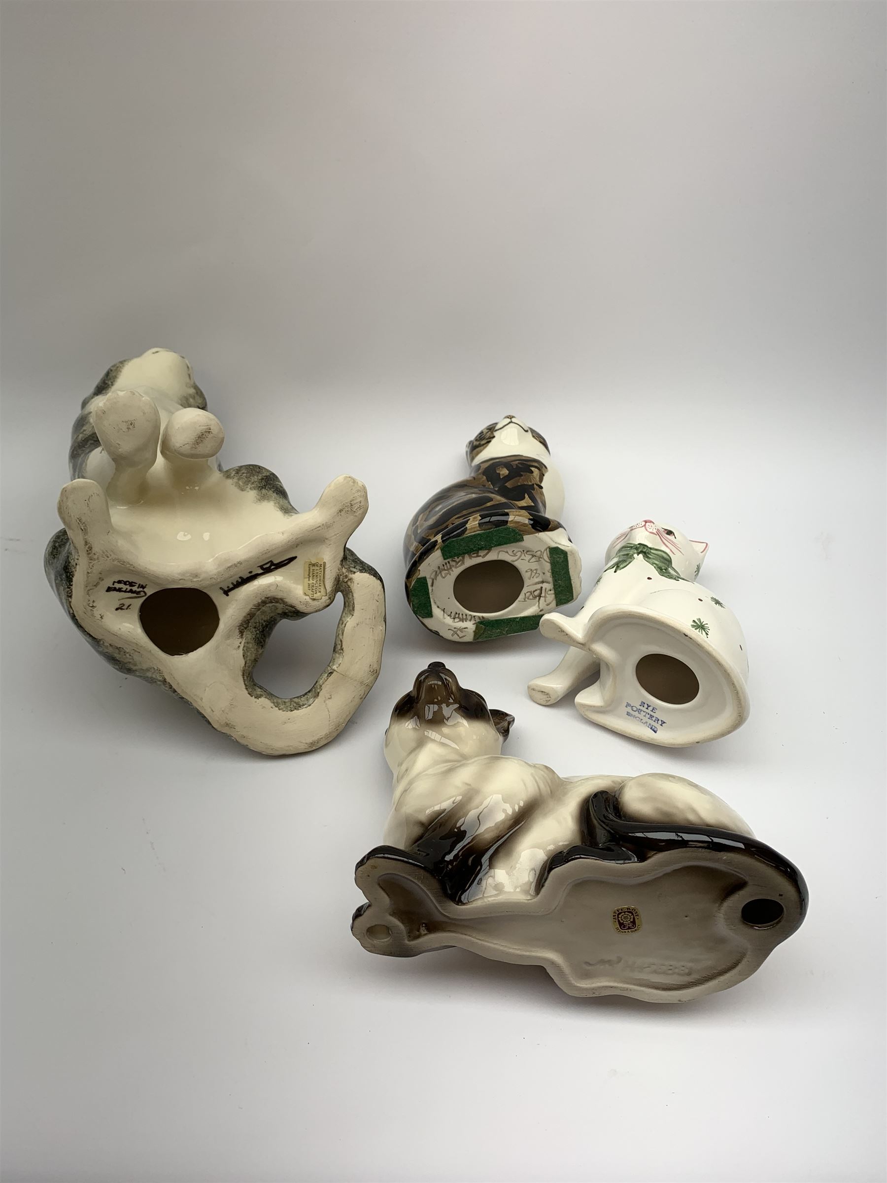 A Winstanley cat, with glass eyes in seated post, signed beneath, H25cm, together with three other figures of cats, including a Rye Pottery example. (4). 