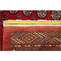 Large crimson ground Afghan Bokhara carpet, the field decorated with repeating Gul and geometric motifs, the multiple guard stripes with further geometric decoration