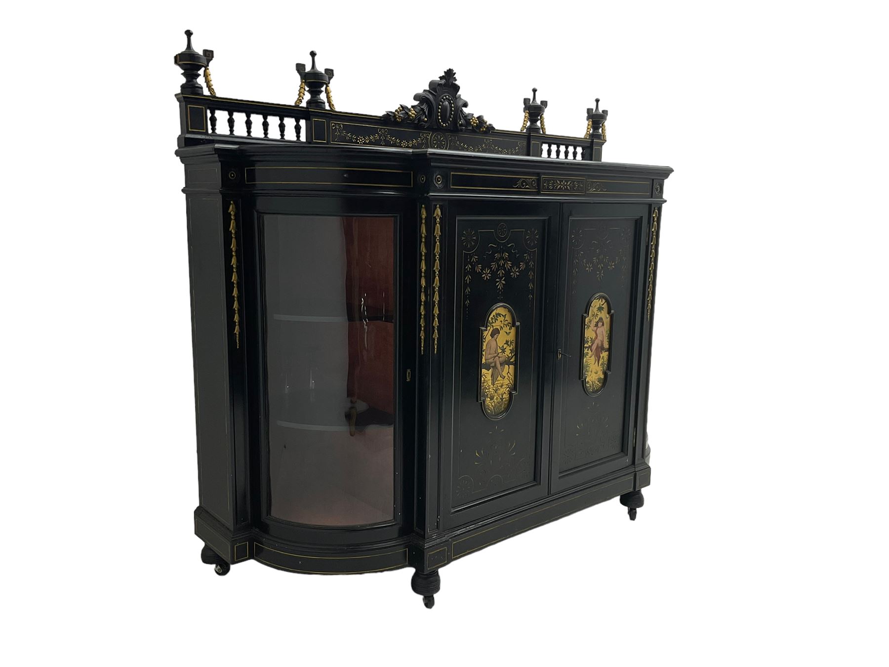 Victorian ebonised credenza side cabinet, raised balustrade back with urn finials and a central carved cartouche, carved and gilded with floral garland decoration, central doors with gilt panels painted with figures sitting over a lake enclosing two shelves, flanked by applied bellflower detail and glazed bow-front side doors, raised on ring turned feet with castors