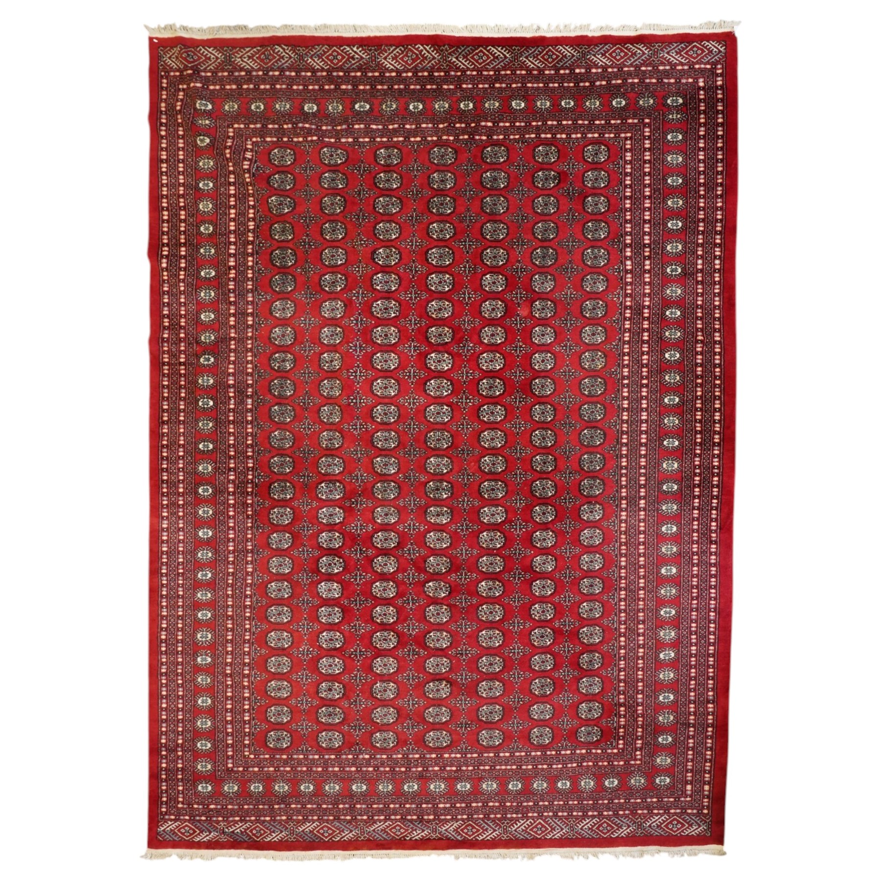 Large crimson ground Afghan Bokhara carpet, the field decorated with repeating Gul and geometric motifs, the multiple guard stripes with further geometric decoration