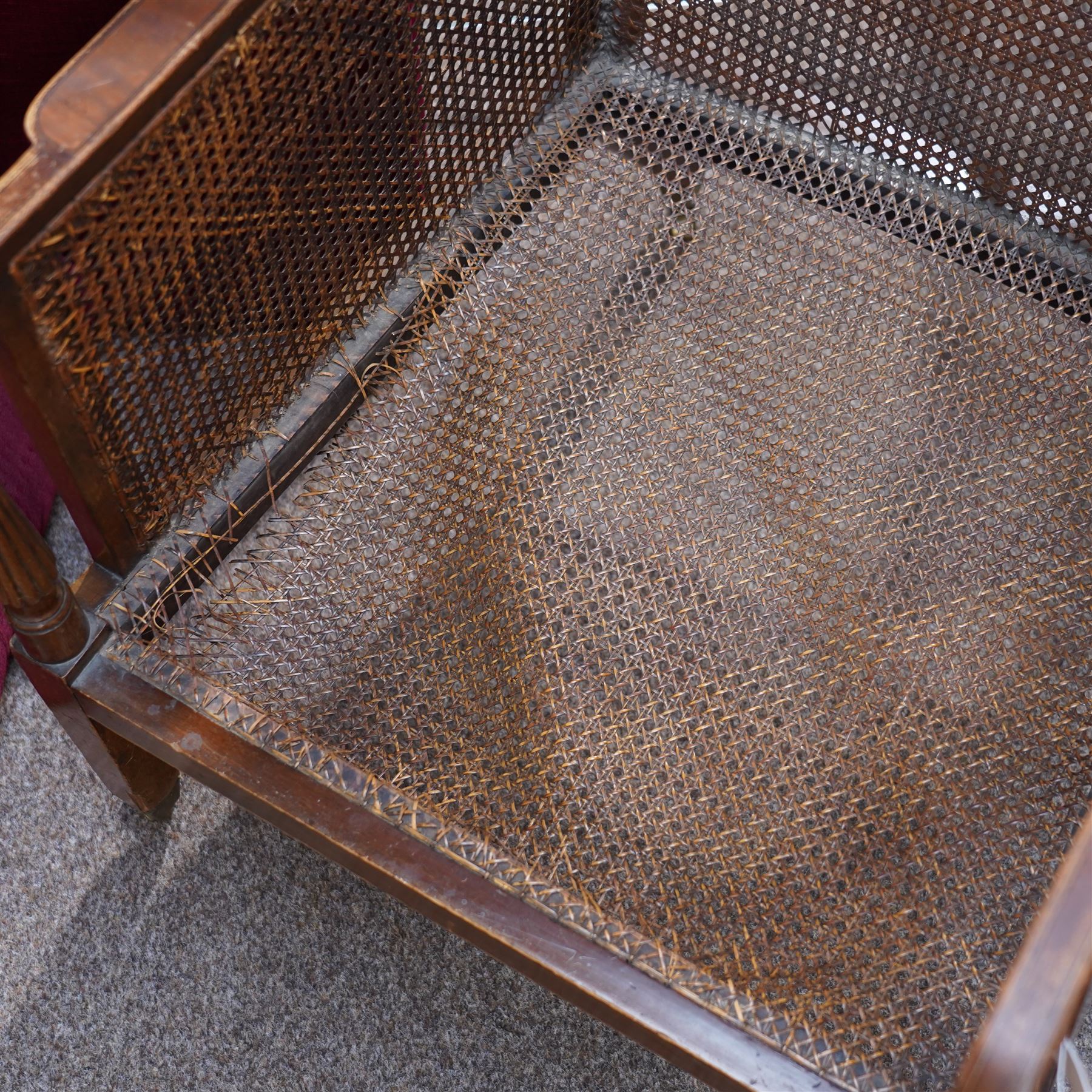 Pair of early 20th-century mahogany Bergère armchairs in the manner of Gillows, the back and seat with woven cane panels with loose red velvet cushions, the frame with swept arms with tapered and reeded uprights, raised on tapered square-section front legs terminating in brass cup castors 