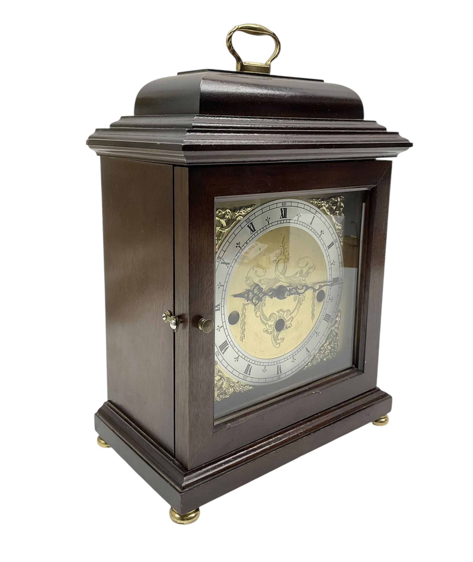 Franz Hermle- 8-day 20th century chiming mantle clock in a mahogany 18th century style case, 
with a bell top and carrying handle, raised on bun feet, brass dial with spandrels and a silvered chapter ring, three train movement striking the quarters on five gong rods, with a floating balance escapement and strike silent feature. With key. 