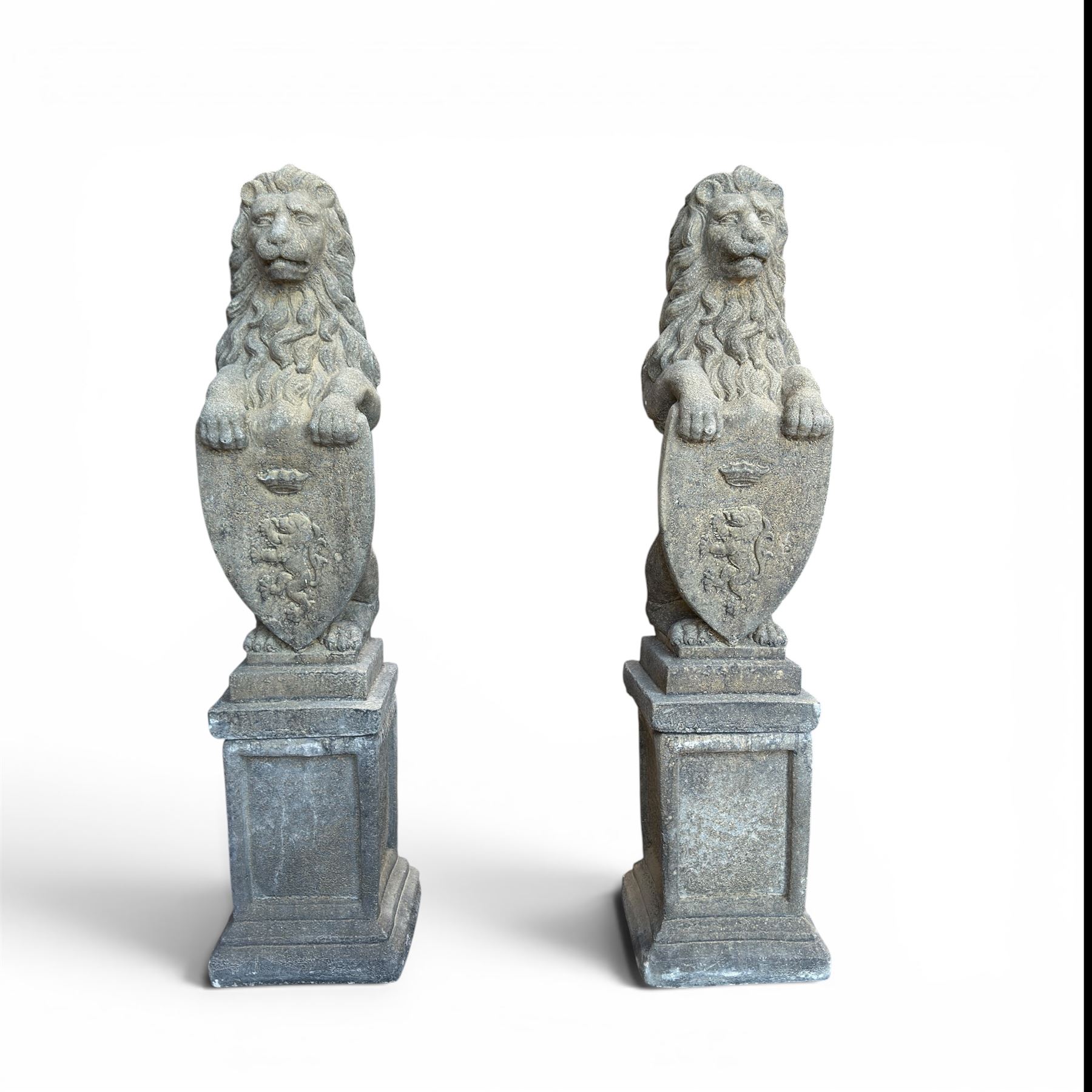 Pair of cast stone Heraldic lions, modelling in upright standing poses with flowing mane, each clasping an Armorial shield moulded with a crowned lion in their forepaws, raised on rectangular pedestals