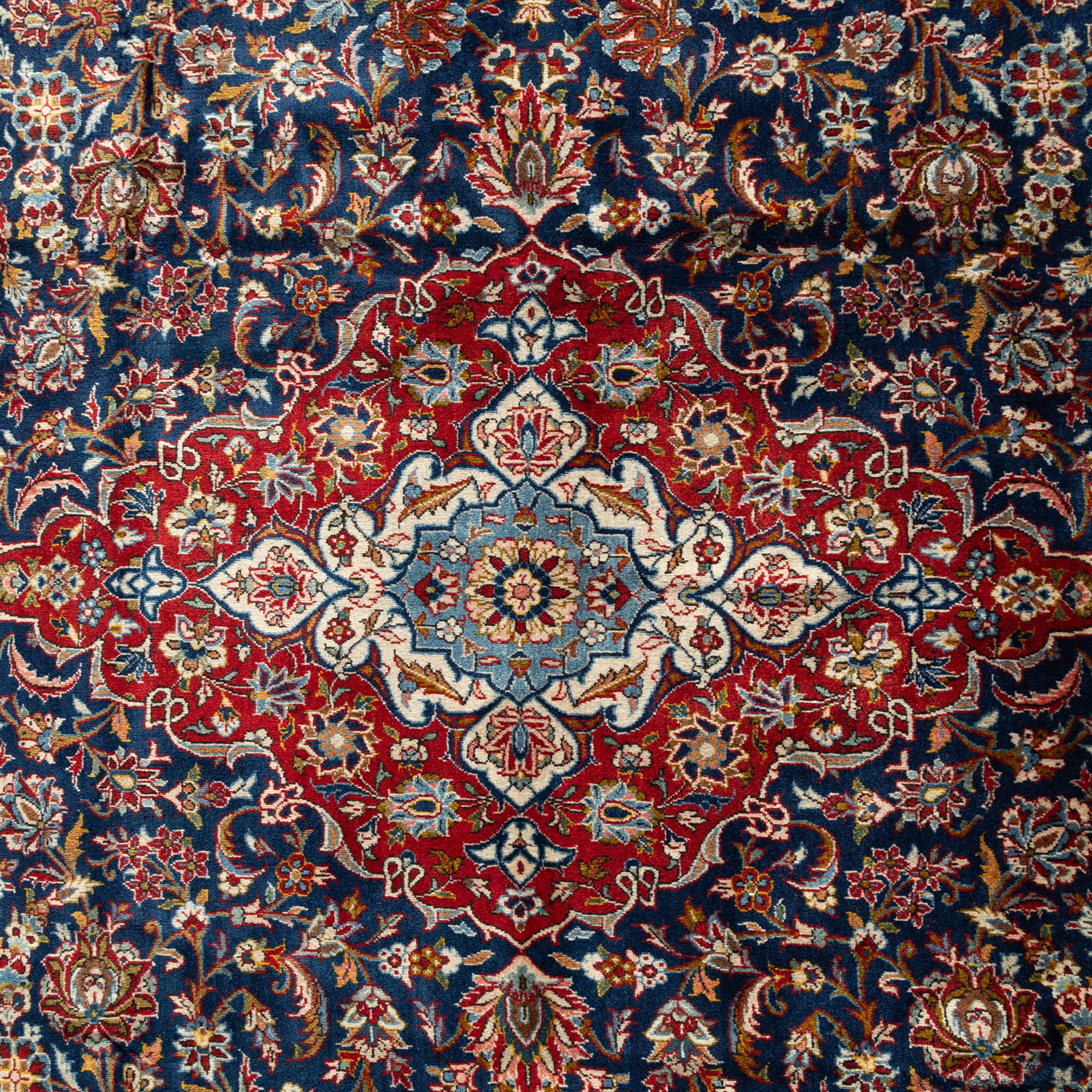 Persian Kashan carpet, navy field with central red diamond medallion enclosing floral rosette, framed by dense scrolling foliage and palmettes, triple borders in red, blue and ivory, originating from central Iran