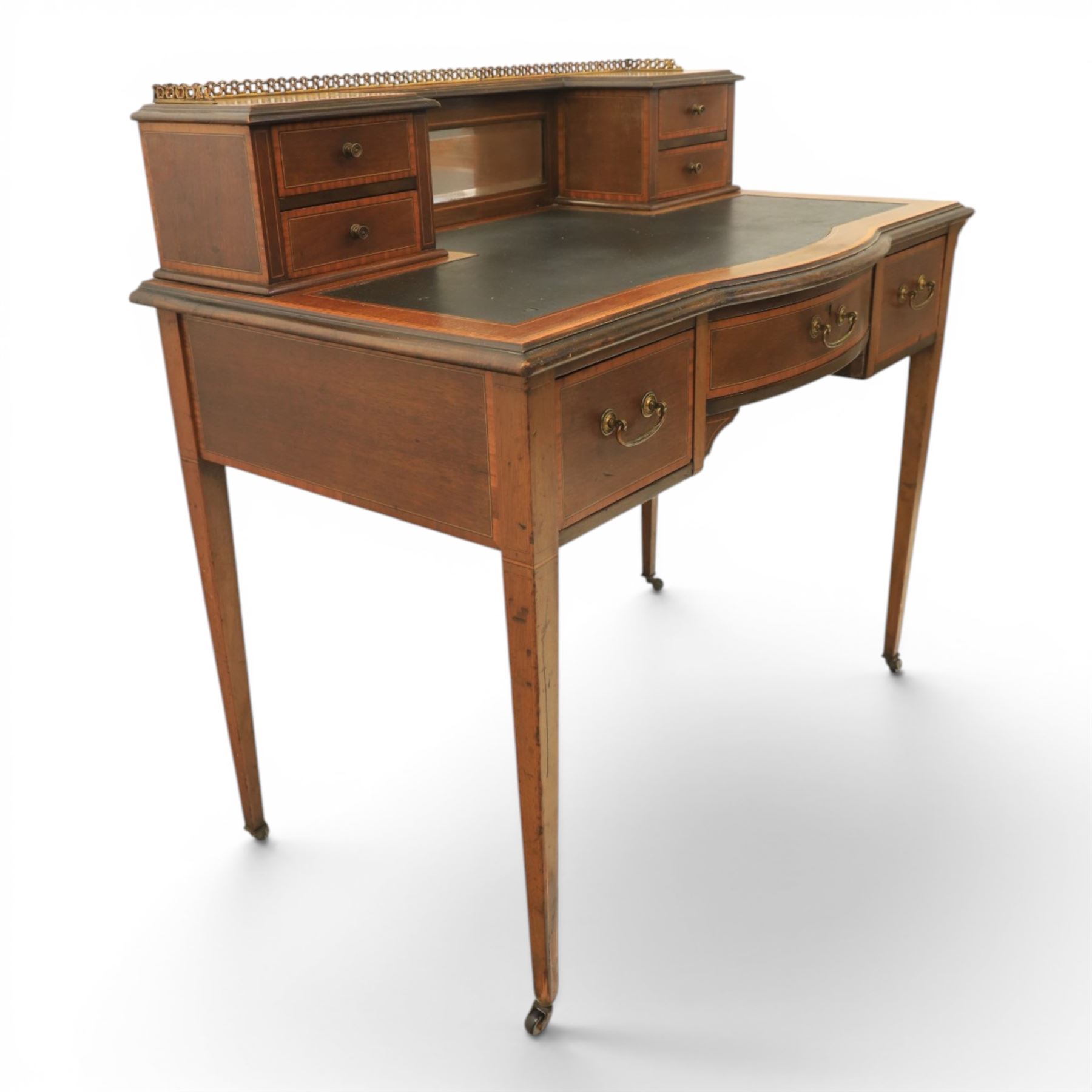 Maple & Co - Edwardian mahogany inlaid writing desk, the superstructure with pierced brass gallery, above an inset mirror and two short drawers, inset leather writing surface, bow fronted with crossbanded drawers and brass swan neck handles, square tapering supports terminating in castors 