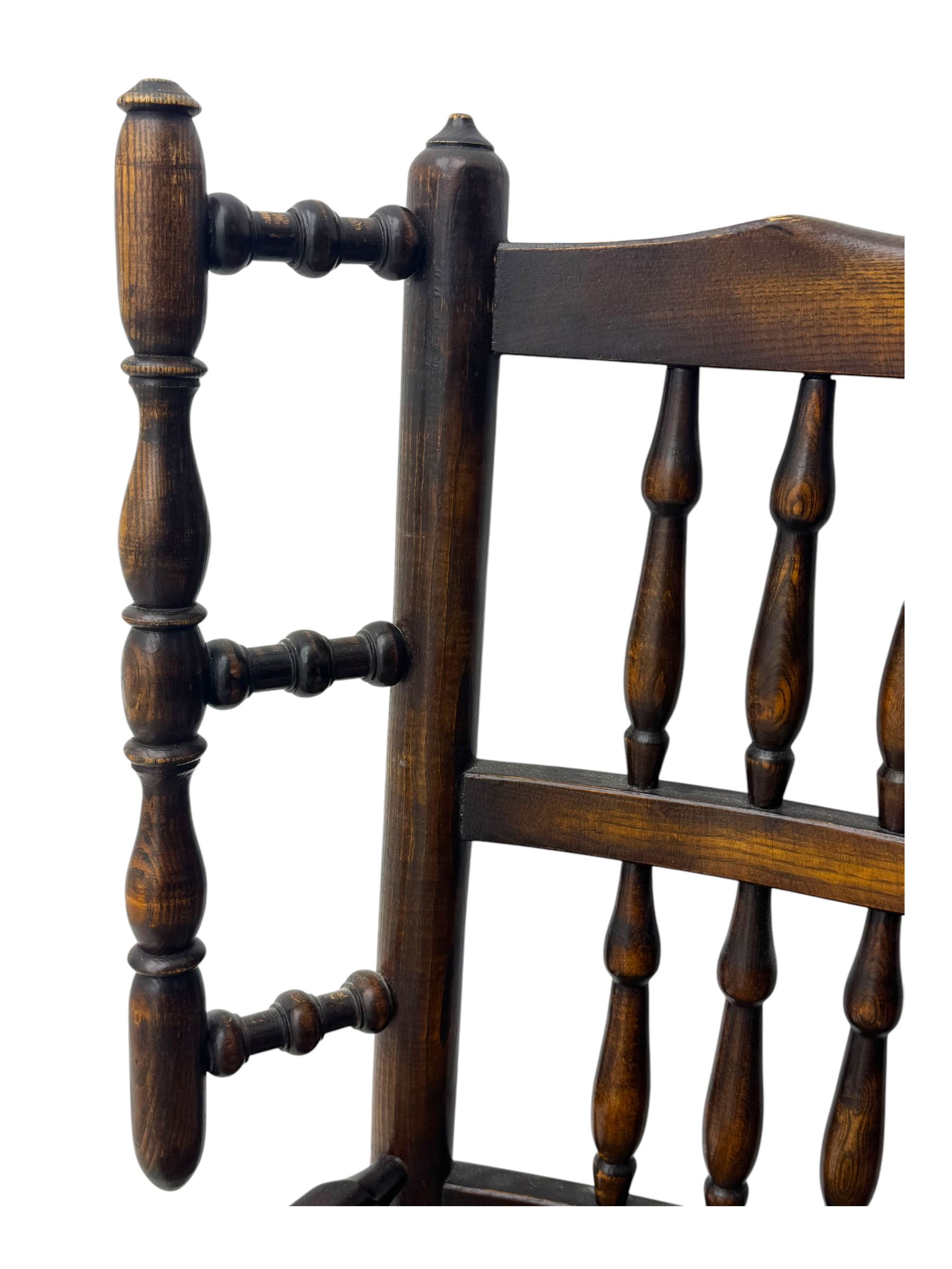 Early 19th century ash armchair, the back with winged spindles extending from a shaped top rail, above a splat of two rows of vertical spindles, with curved arms and a rush seat, raised on turned supports united by double stretchers terminating in castors