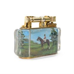 Rare one off special commission Dunhill Sporting Horse Racing half-giant 'Aquarium' table lighter, circa 1955, the lucite panelled body engraved in reverse intaglio technique and hand-painted with Nicholas Nickleby in action, winner of the Royal Hunt Cup, Ascot June 1955, the reverse with jockey Willie Snaith mounted upon Nicholas Nickleby, the gold plated top with arm stamped Dunhill Reg. No 737418, the base stamped DUNHILL LIGHTER, H7.5cm W10cm D5cm

Provenance:
Commissioned by the owner of Nicholas Nickleby, the lighter was gifted to Colin Hetherton, a young veterinary surgeon whose intervention saved Nickleby from certain retirement. Hetherton’s expert care and persistence brought the horse back to full health, culminating in a win that stunned the Ascot crowd.