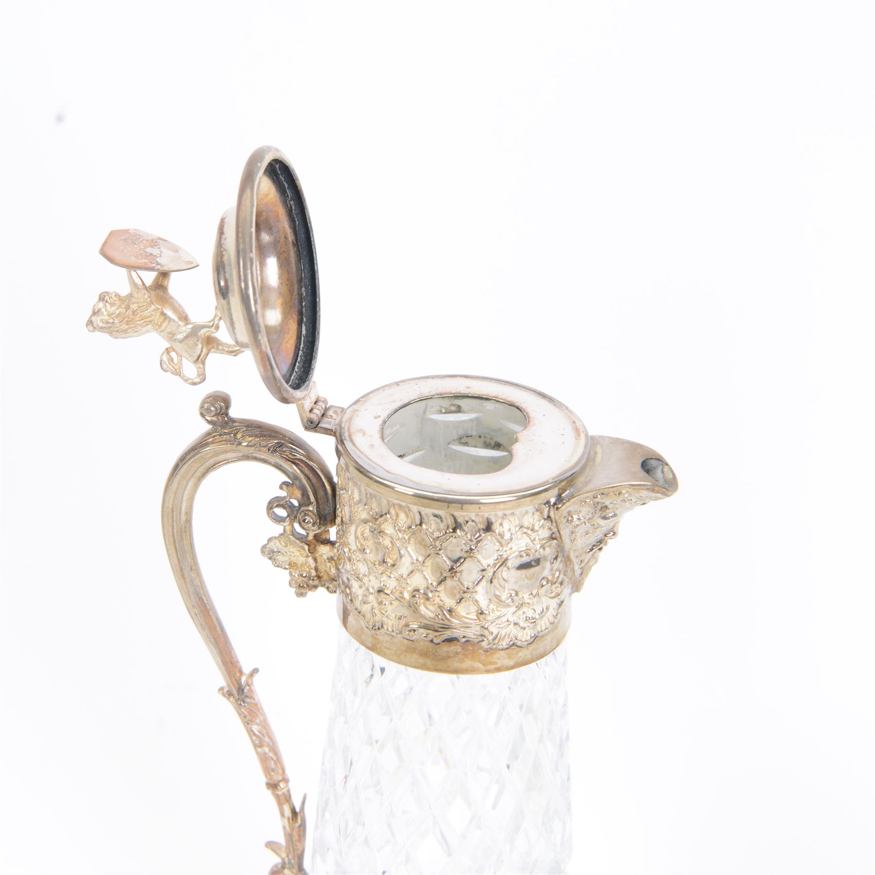 Silver plate mounted glass claret jug, the glass body of tapering form, the hinged lid a lion finial with shield shaped empty cartouche, the collar and spout cast with Bacchus face masks surrounded by grapes and vines, together with another silver plate mounted example, tallest H33cm